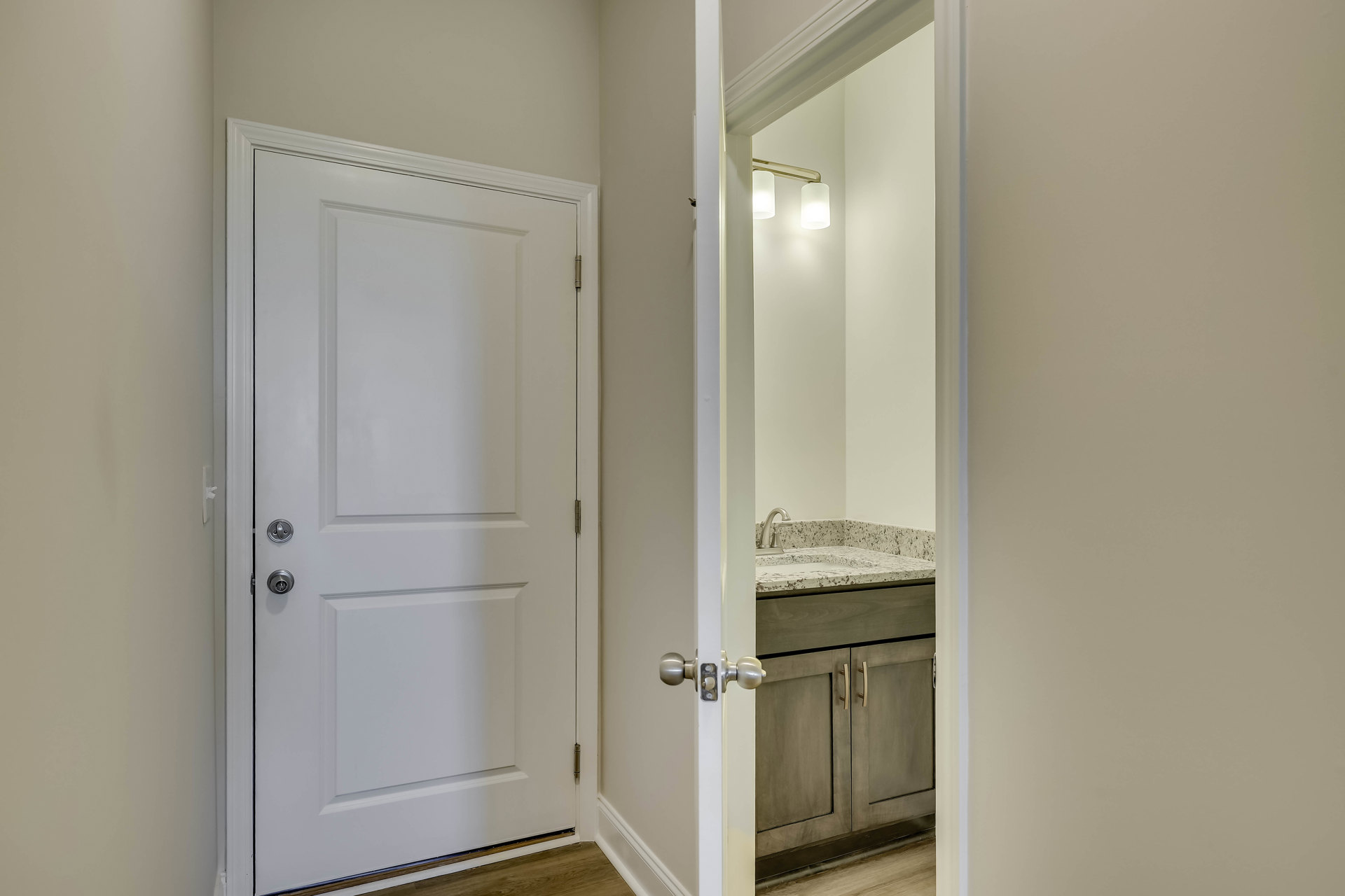 White bathroom with rectangular sink, white door featuring silver handle, tiled floor, and white walls