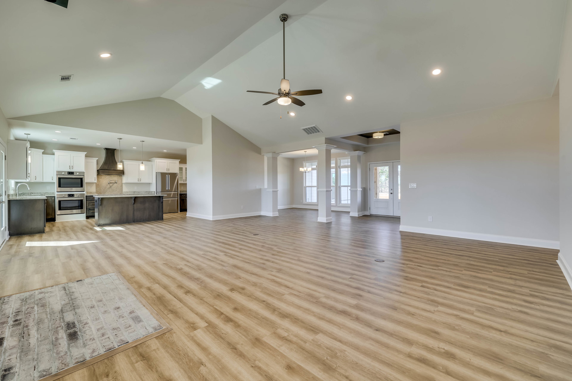 Spacious room with wood flooring, stainless steel oven, white door with glass panes, ceiling fan with light fixture, and neutral plaster walls