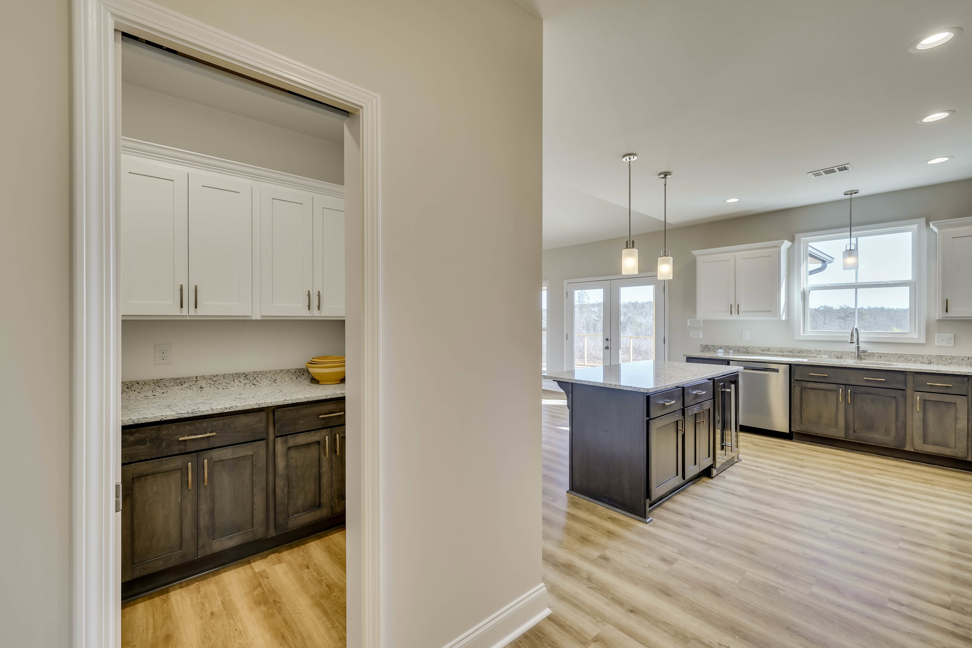 Kitchen with wood flooring, white cabinets, marble-topped island, stack of yellow bowls, ceiling light, window, and white door with black trim.
