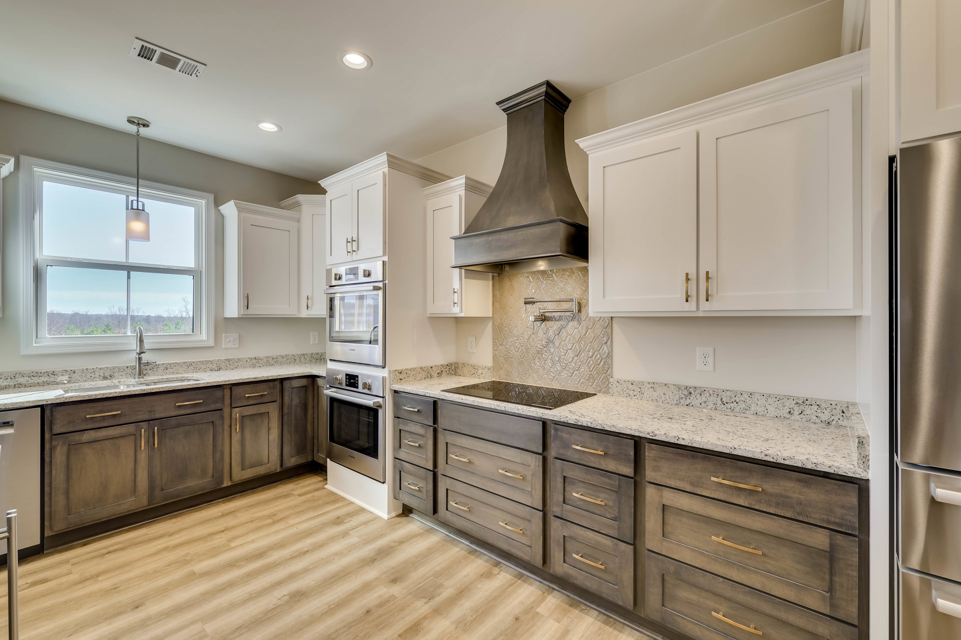 White kitchen with granite countertops, stainless steel stove beneath a large brown vent hood, window with ceiling light, close-up views of silver surface and drawer.
