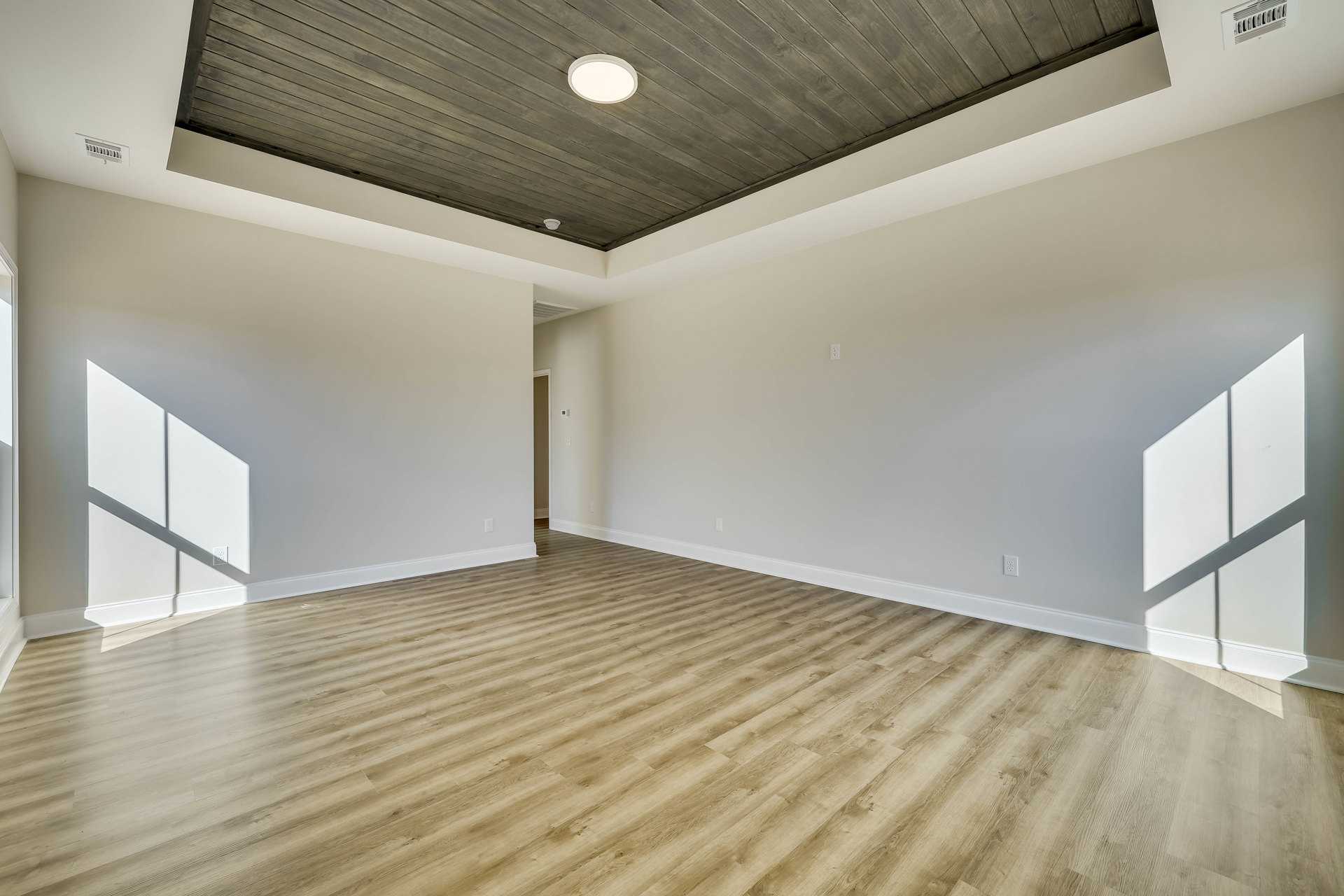 Wood plank flooring and matching wood ceiling, white plaster walls, ceiling-mounted light fixture, close-up of air vent, rectangular white object against grey background