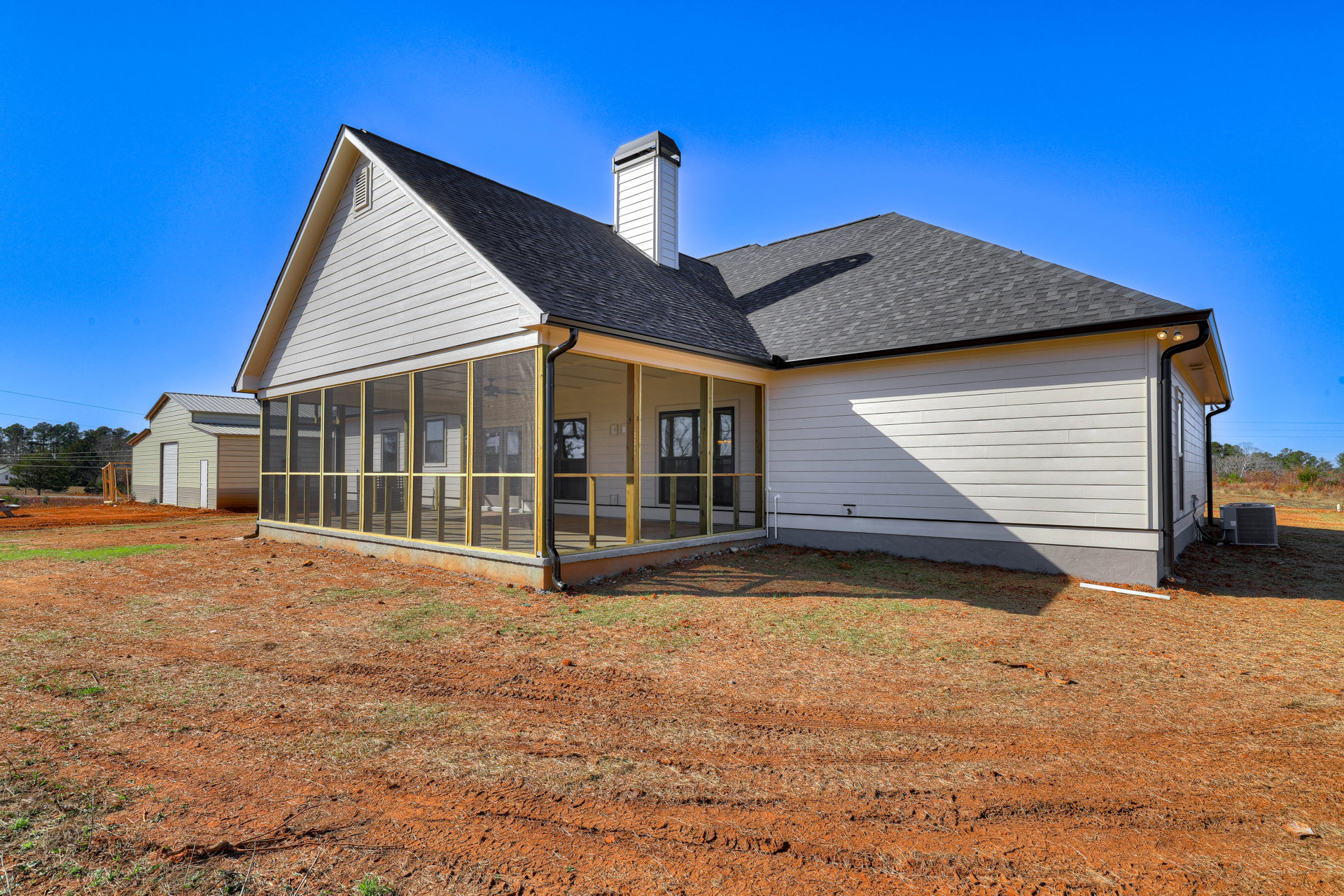 Two-story farmhouse with white siding, covered front porch, white chimney, and large windows; shaded by nearby trees.