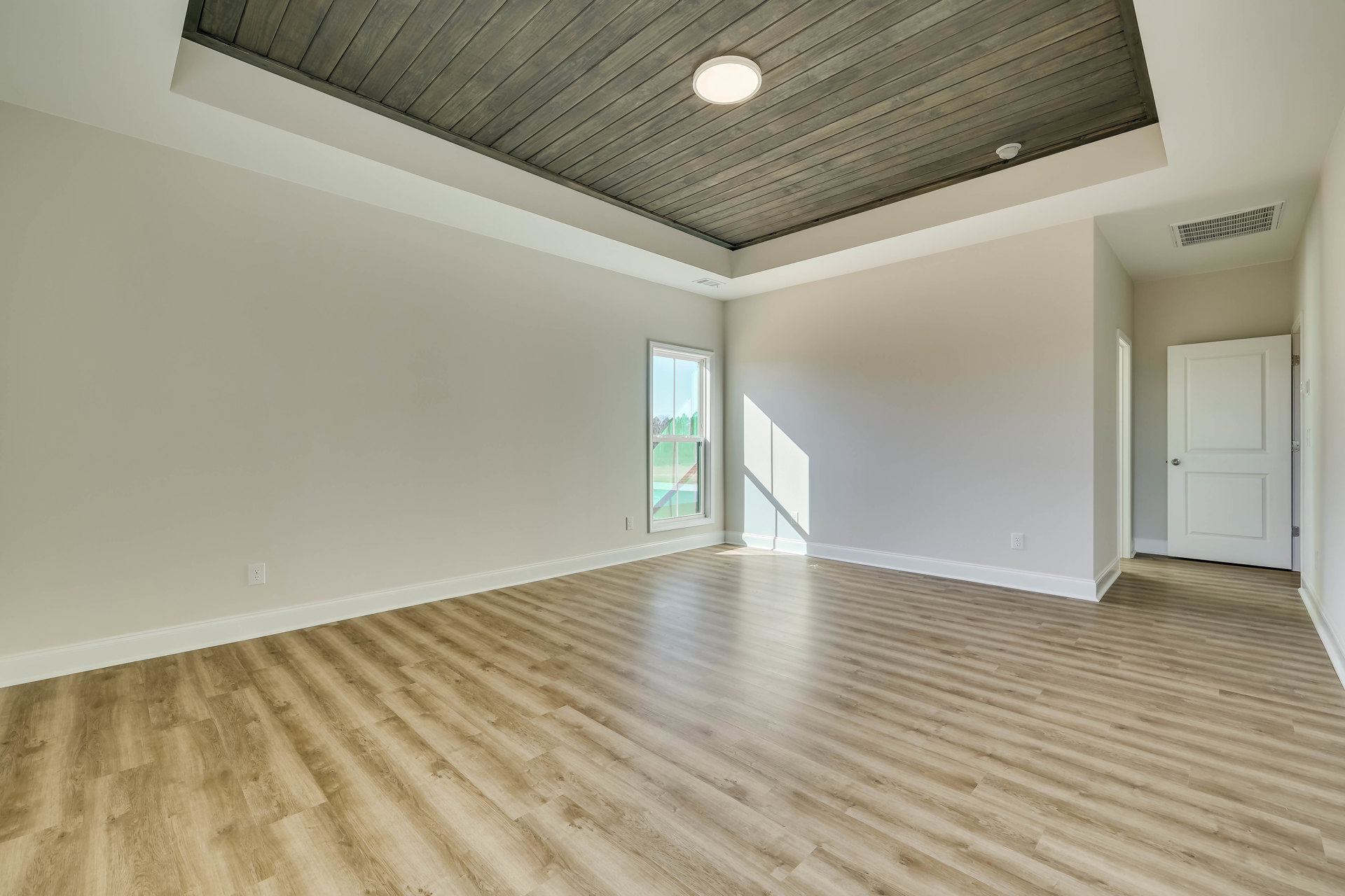 Wood floor and wood ceiling in a room with white-framed window, white door with silver knob, and ceiling light fixture