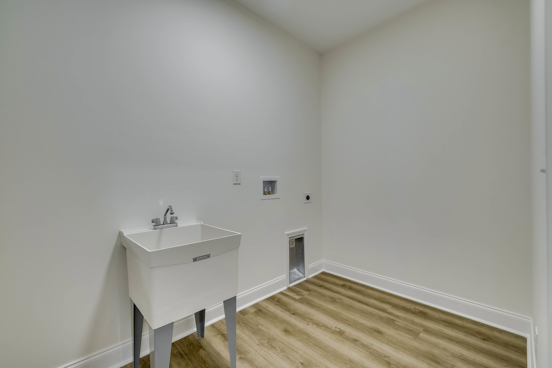 White bathroom with plaster walls, wood flooring, and a white sink featuring a silver faucet and metal drain.