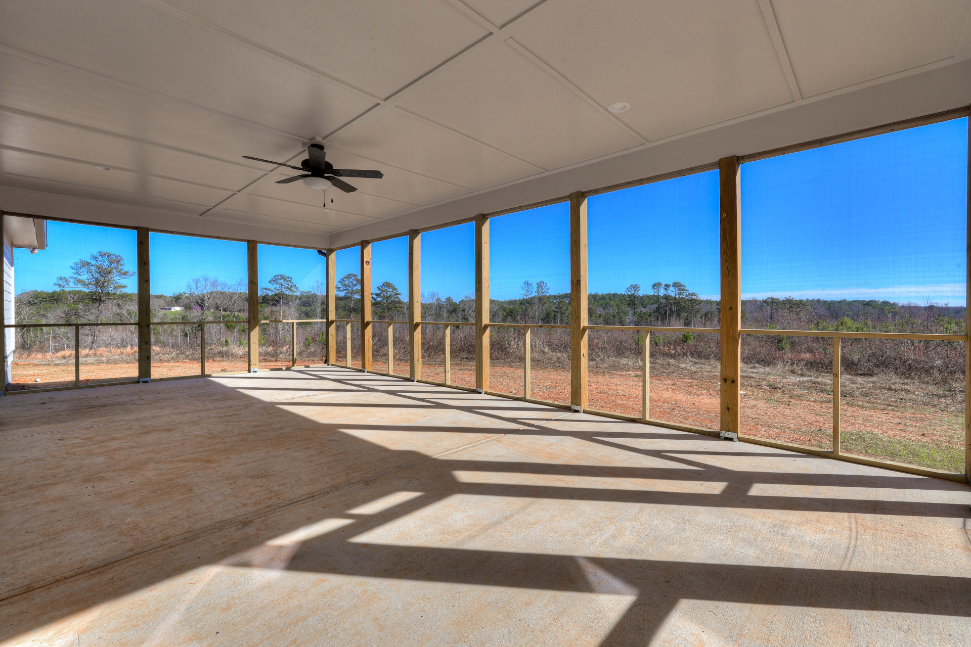 Covered porch with wood railing, ceiling fan with light, large windows, and shaded outdoor area