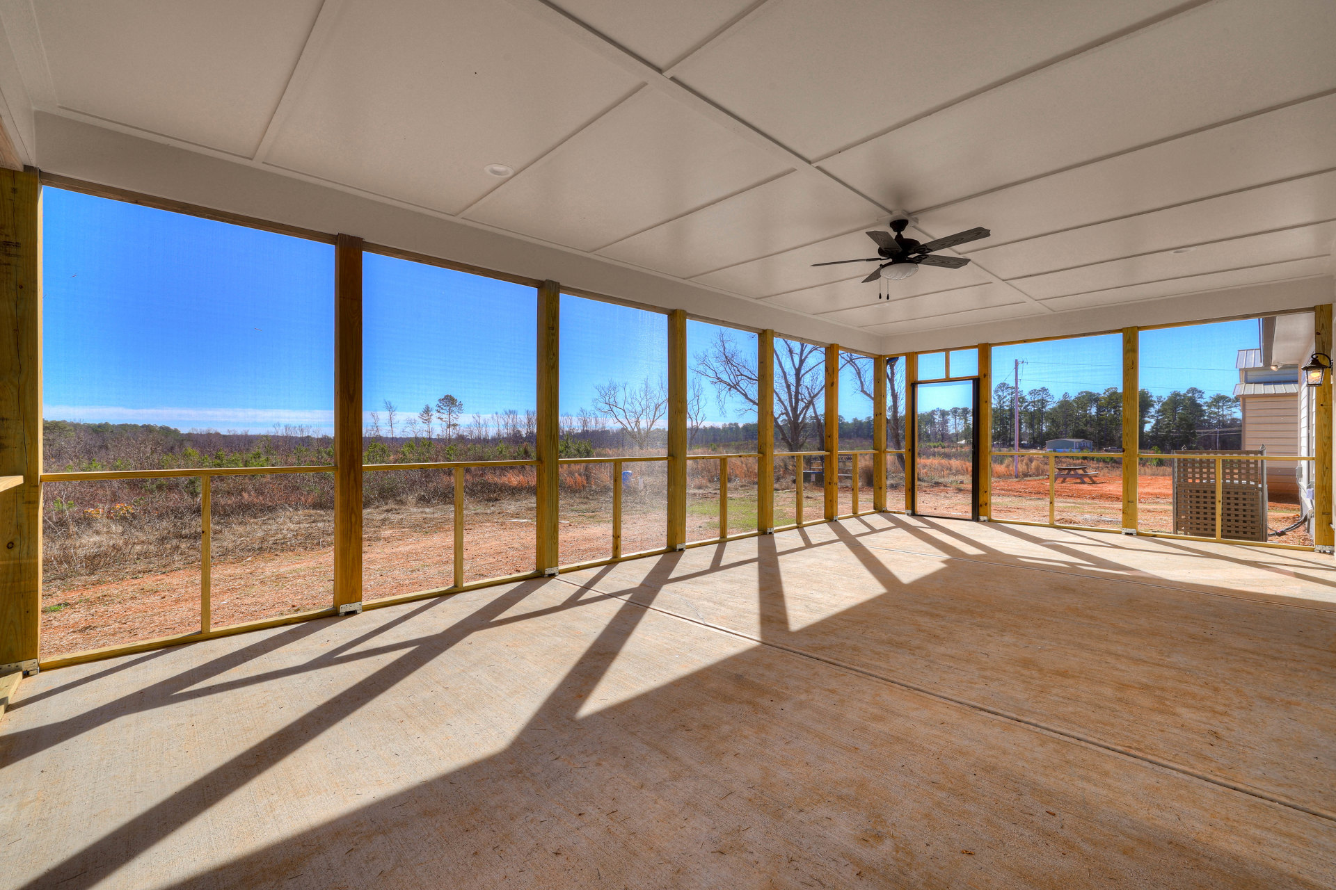 Spacious room with concrete floor, ceiling fan with light, large window, and view of wooden fence with yellow accent bar