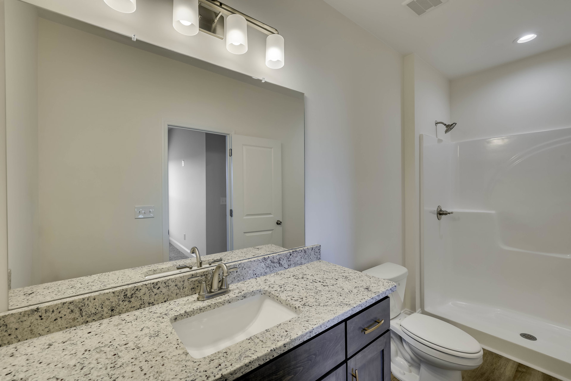 Marble countertop vanity with silver faucet, white toilet with closed lid, light fixture illuminated above, white walls and tile flooring, light switch visible near sink