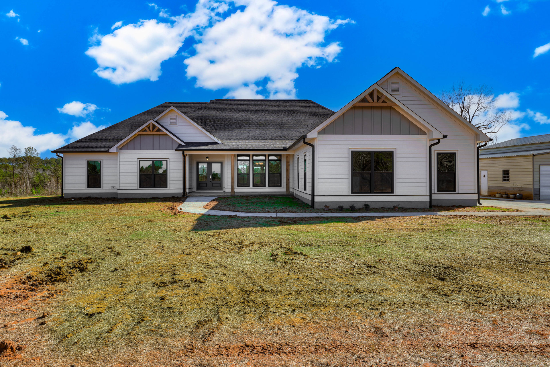 Modern home with black-framed windows, dark roof, manicured green lawn, and blue sky with scattered clouds