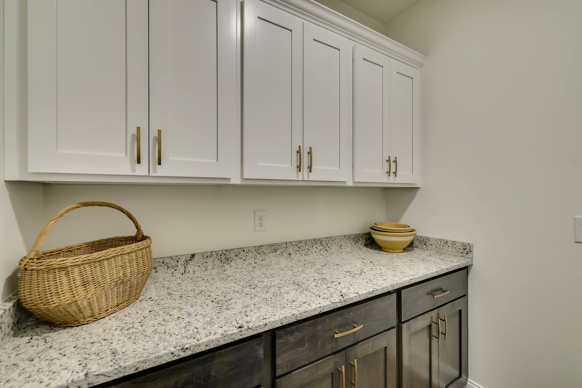 White kitchen cabinets and marble countertop with a woven basket and stacked bowls, stainless steel sink, and drawers visible.