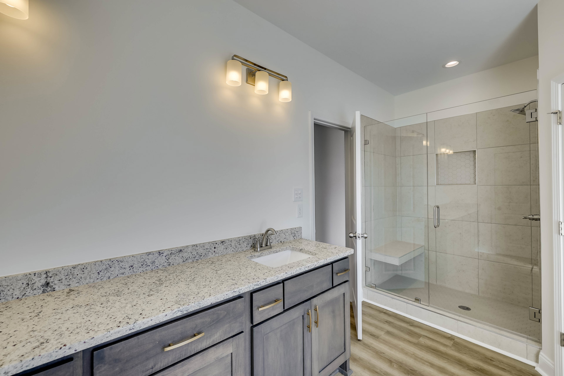 Modern bathroom featuring a glass-enclosed shower, white ceramic sink set in a stone countertop with wood cabinetry, and a three-light fixture mounted above a large mirror.