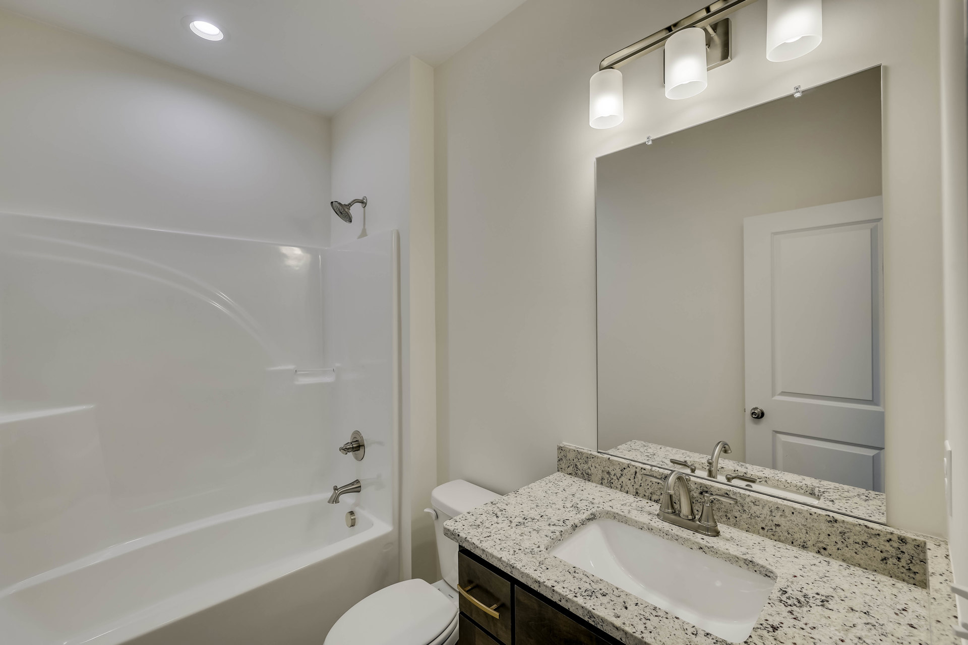 Modern bathroom with white porcelain sink on marble countertop, chrome faucet, wall-mounted toilet, glass-enclosed shower with round showerhead, freestanding white bathtub with