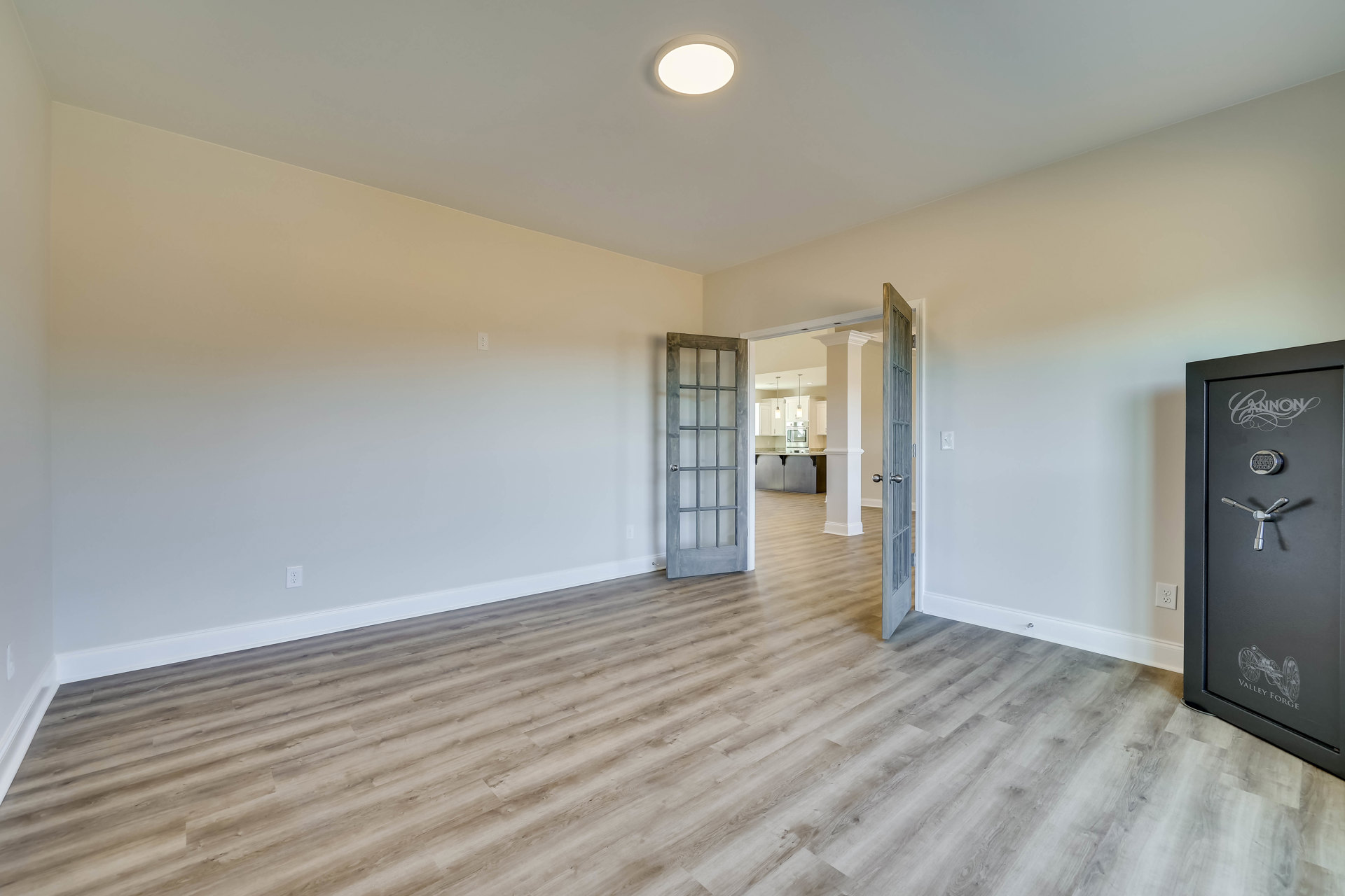 Wood floored room with open door featuring glass panes, white plaster walls, ceiling light fixture, and visible safe with combination lock