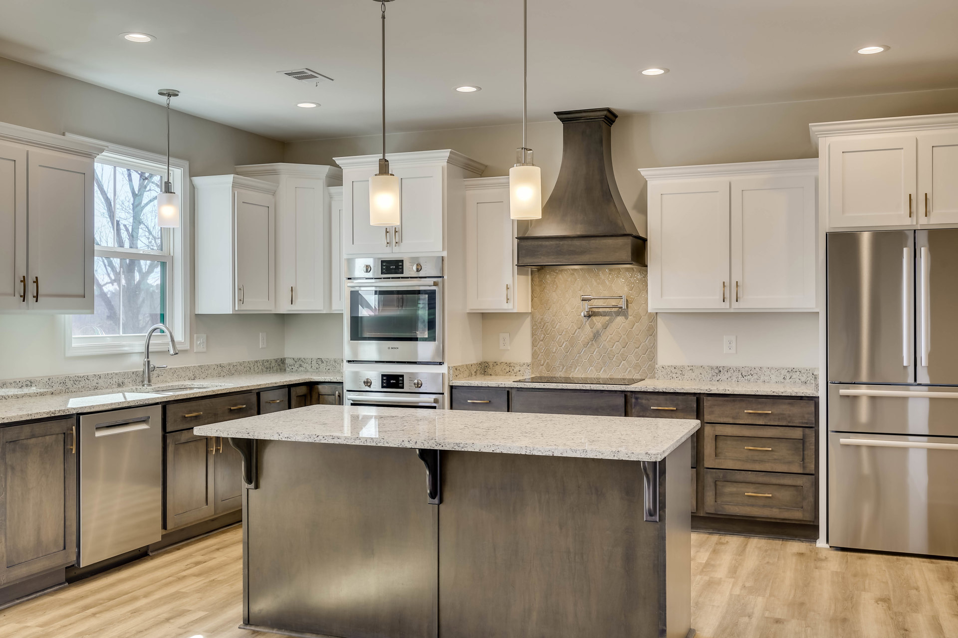 Spacious kitchen featuring a large granite island, stainless steel stove with glass door, silver refrigerator with black handle, wood cabinetry, and light-colored countertops.