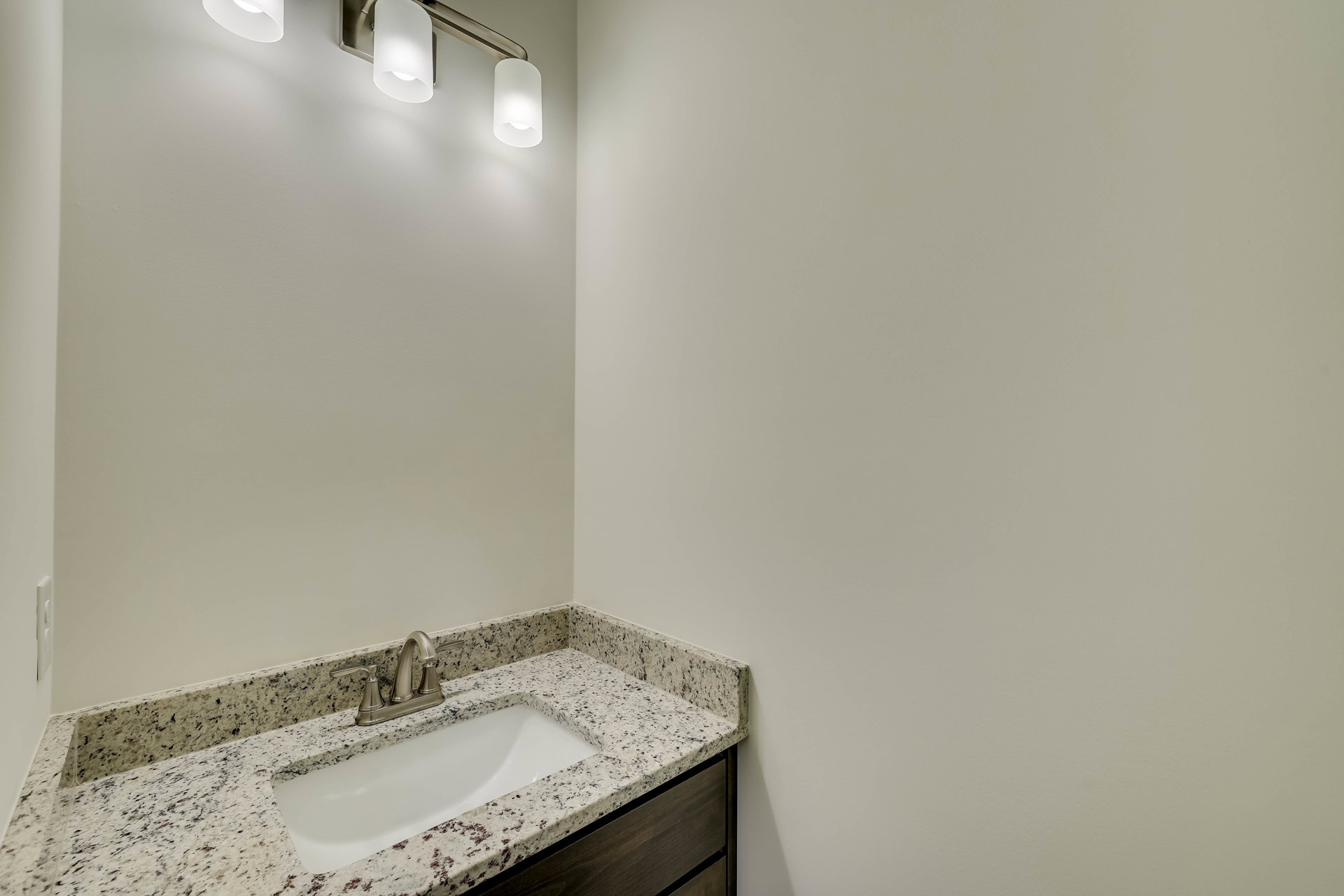 Undermount sink with chrome faucet set in a marble countertop, white tile backsplash, and modern light fixture with white shade above
