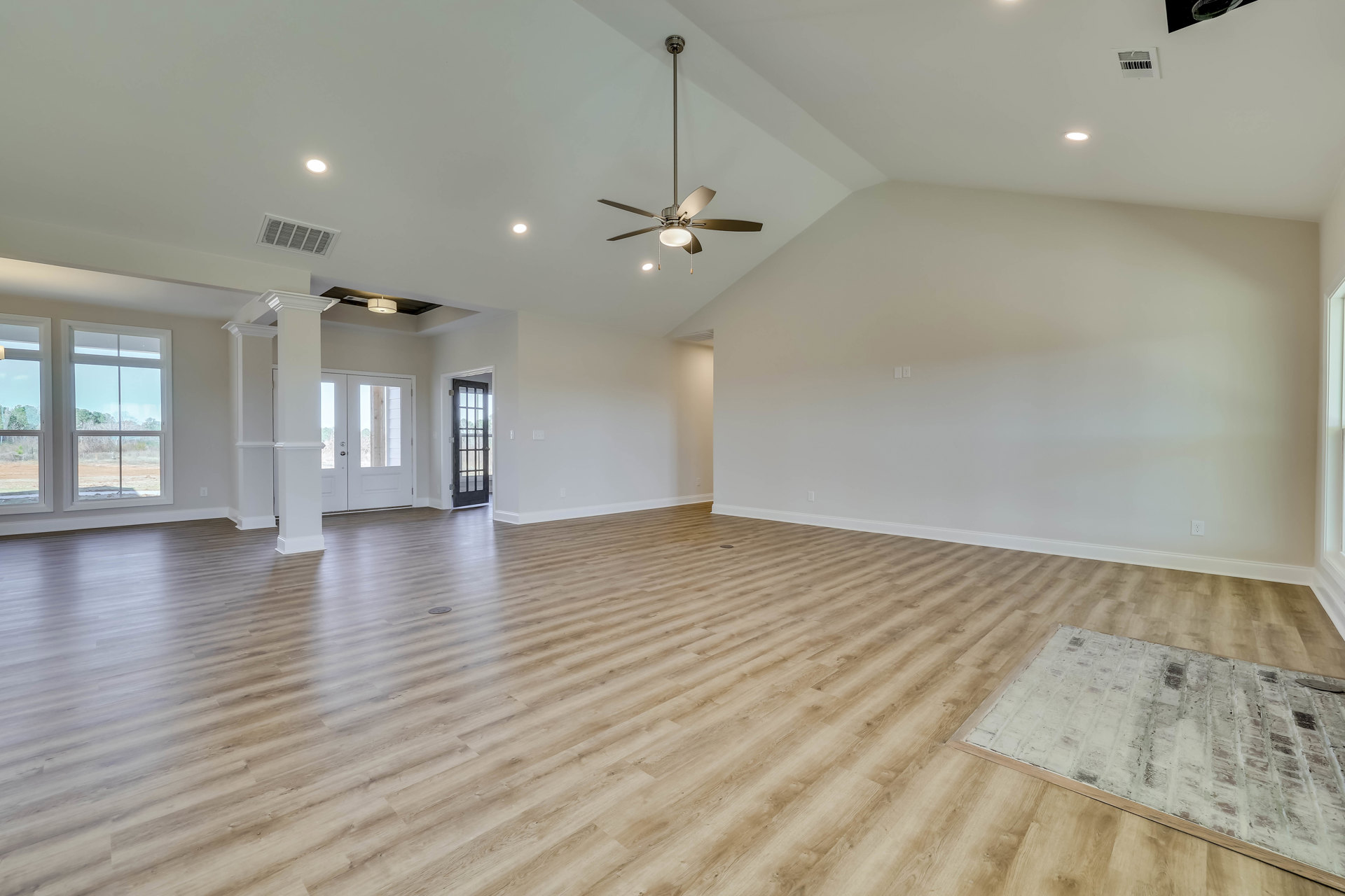 Spacious room with hardwood floor, ceiling fan, white brick accent, glass-paneled door, and window overlooking a field