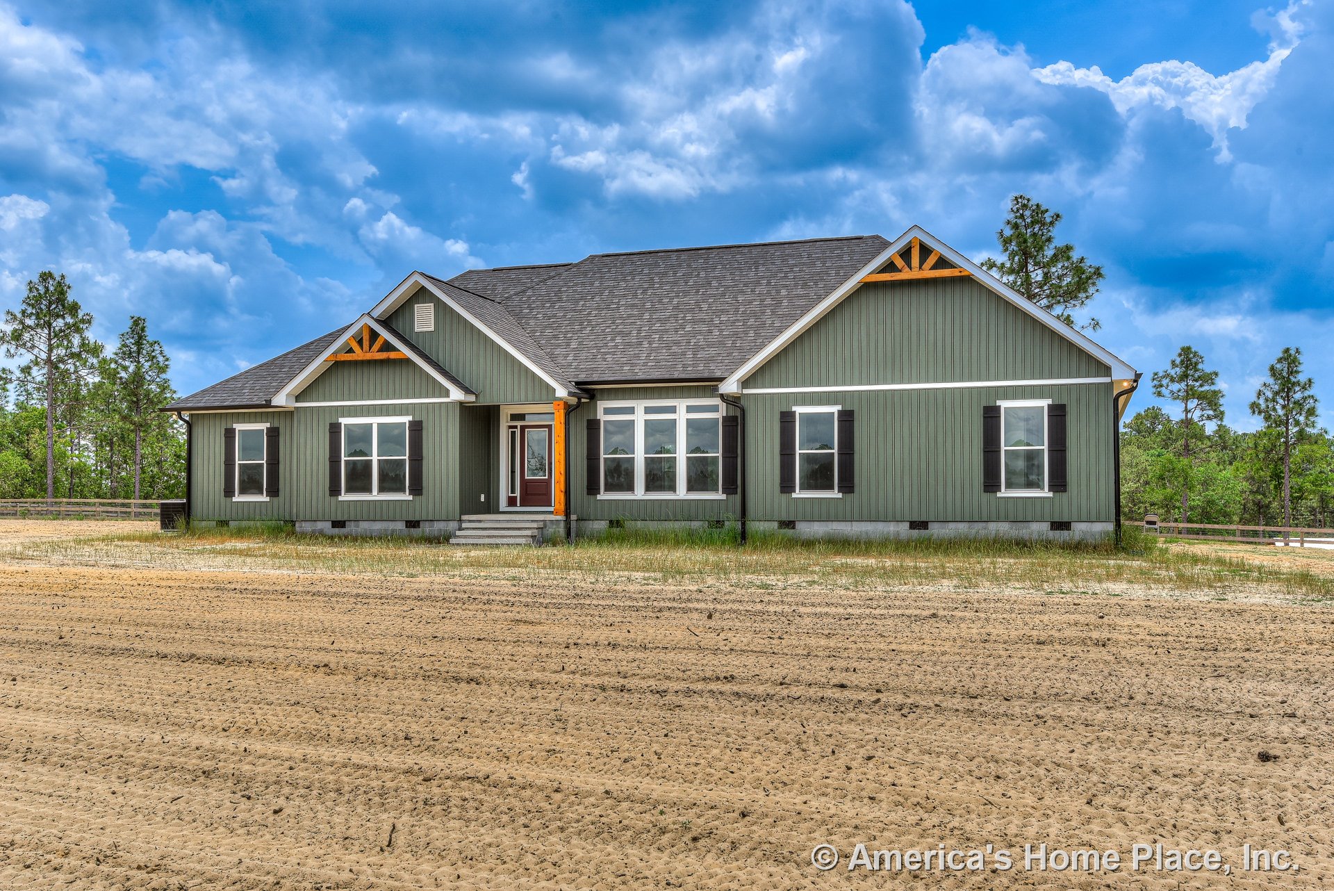Green vertical siding with black shutters, decorative wood gable trusses, covered front porch, multiple double-hung windows, gray shingle roof, white trim accents, single-story