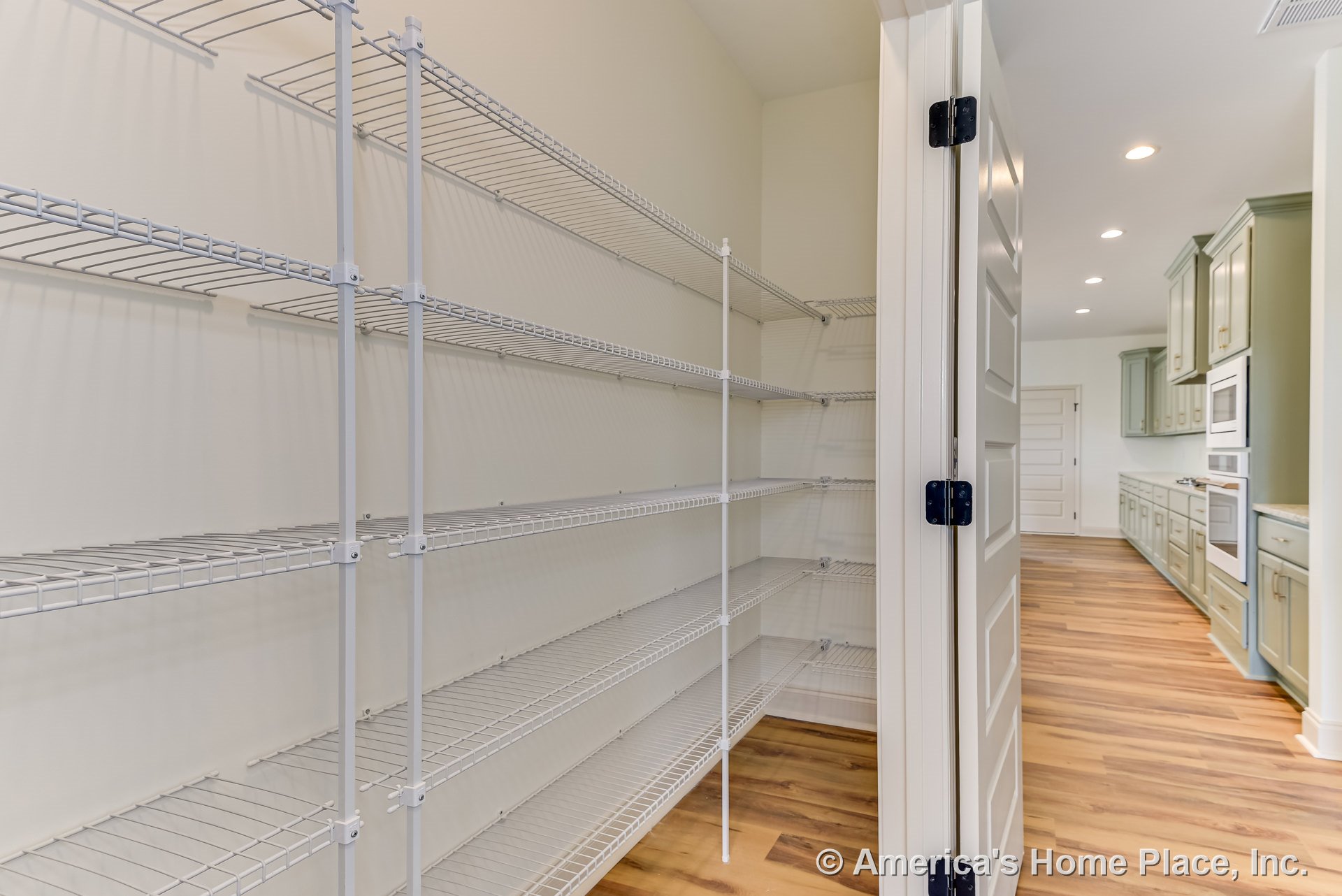 Walk-in kitchen pantry with built-in white wire shelving, folding door, adjacent cabinetry, wood-look flooring, and recessed ceiling lights.