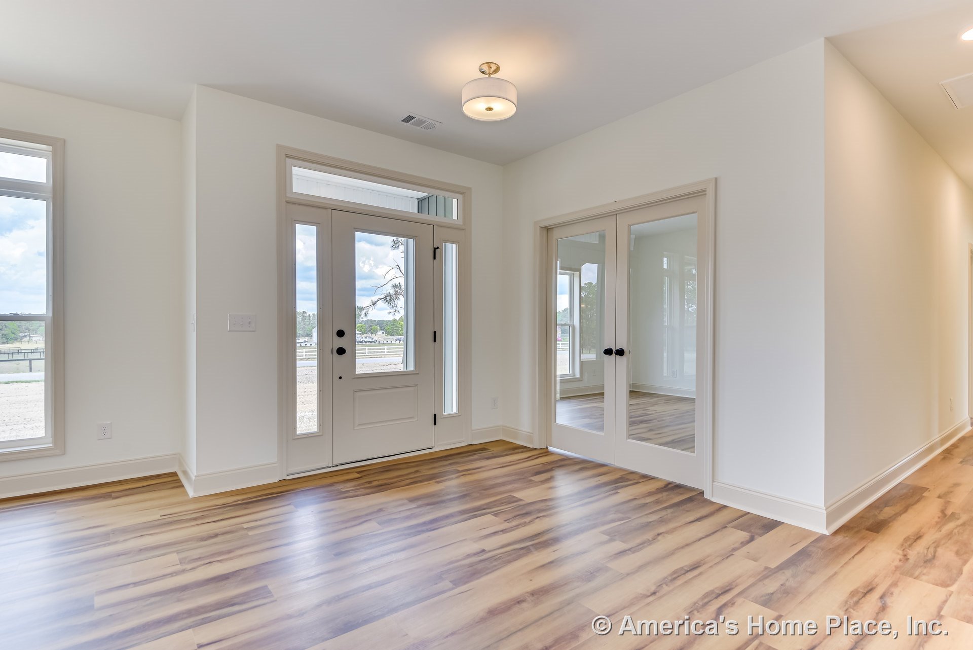 Glass-paneled front door and double interior doors with mirrored glass, large windows with trim, light wood-look flooring, white walls and ceiling, flush mount ceiling light
