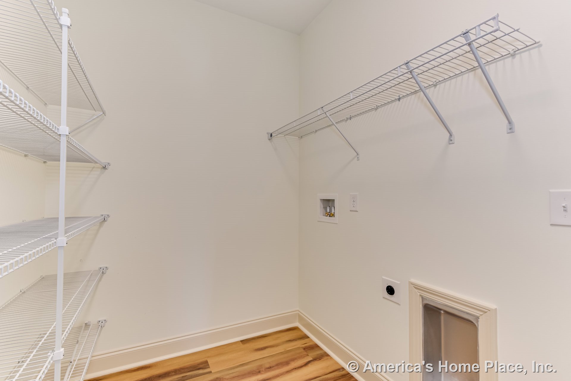 Laundry room with wire wall shelving, washer and dryer utility hookups, wood-look vinyl flooring, white baseboard trim, wall outlet, built-in storage, and pet door.