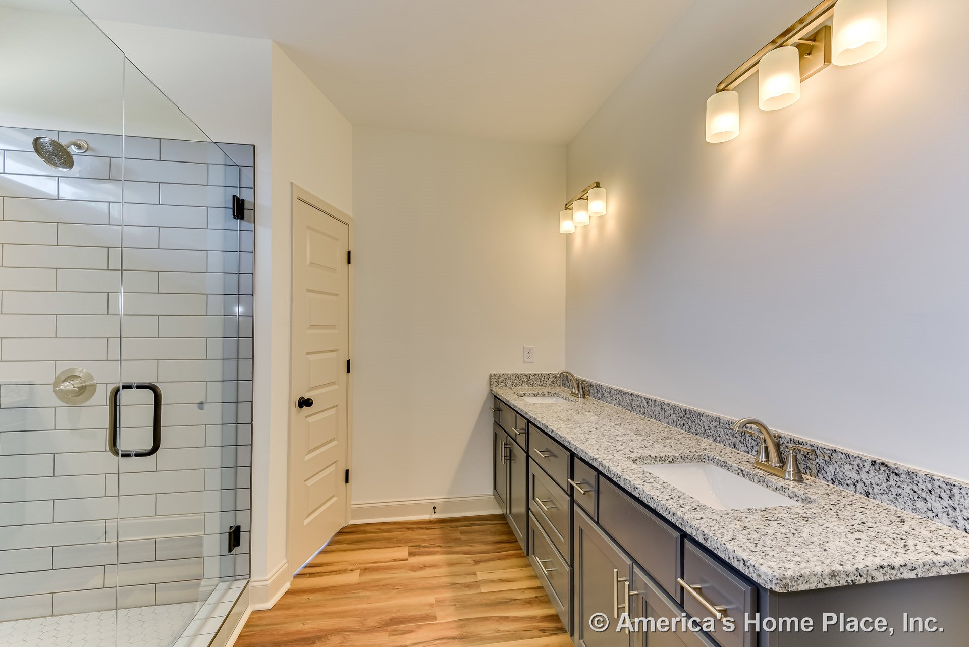 Glass-enclosed shower with white subway tile walls, granite double vanity with undermount sinks, dark cabinetry featuring brushed hardware, wood-look plank flooring, and