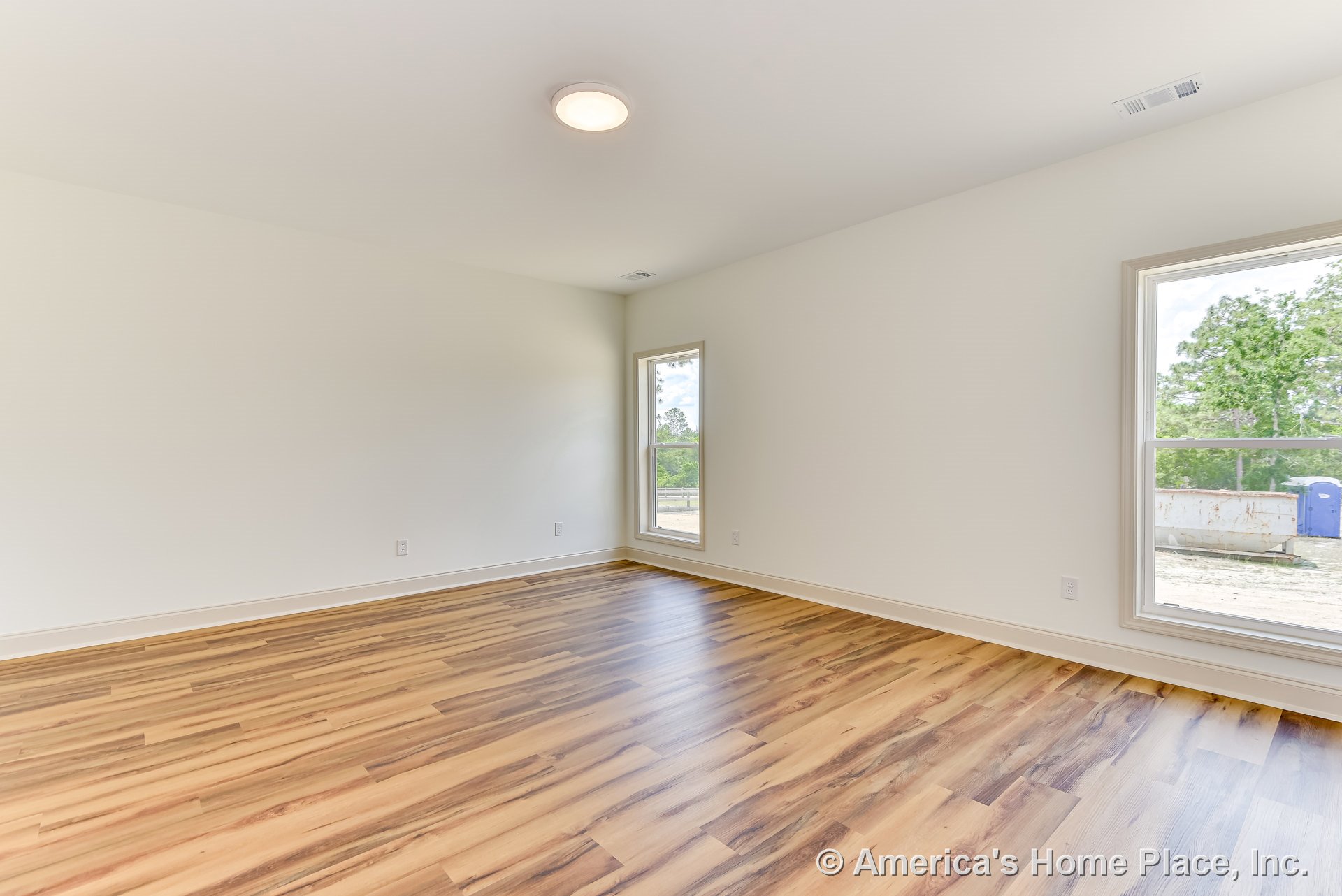 Spacious rectangular room with large windows, light wood-look flooring, white walls, baseboard trim, and flush ceiling light, showcasing modern finishes and abundant natural light.