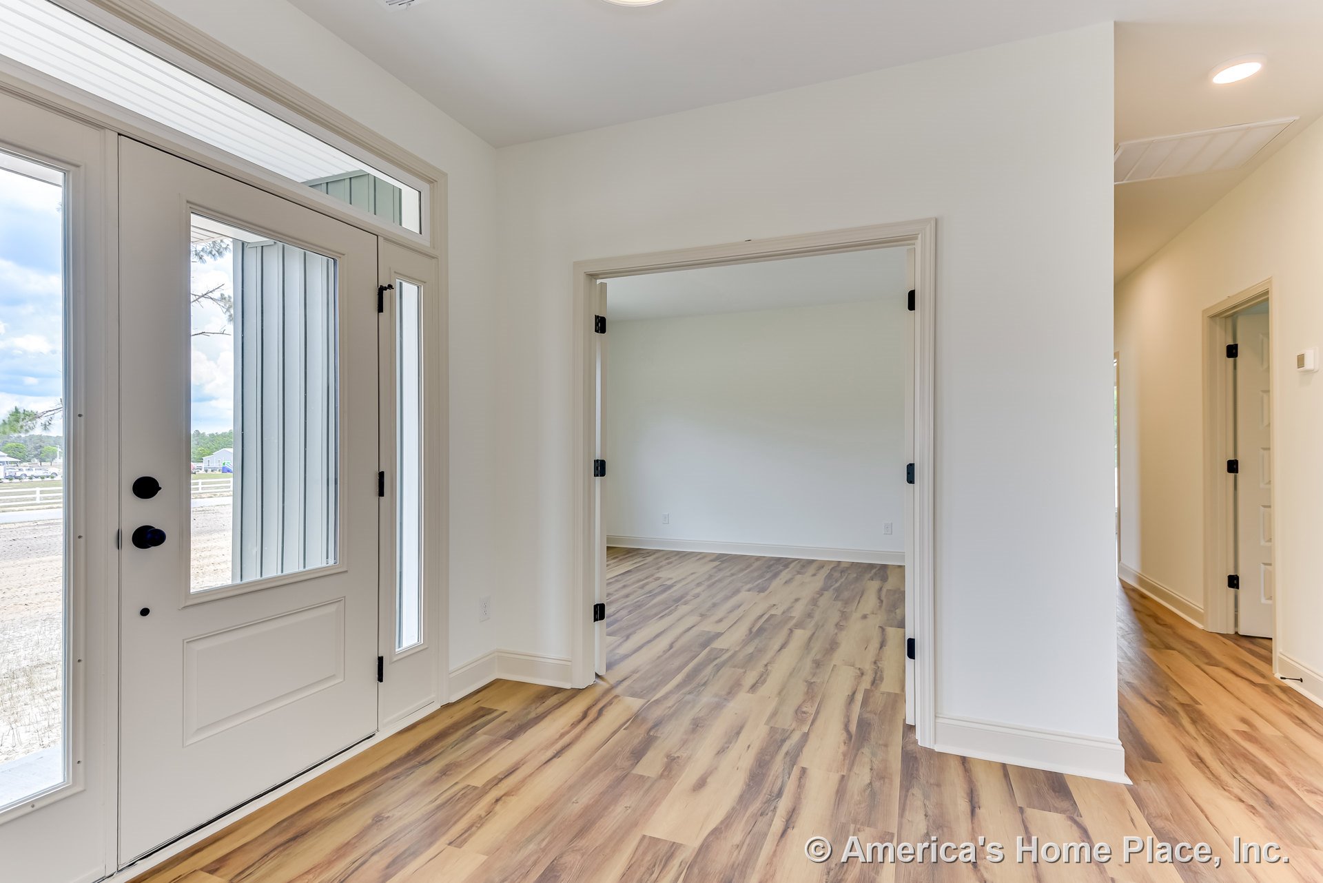 Glass-paneled front door with sidelights and transom window opens to foyer featuring wood-look flooring, wide baseboard trim, double interior doors, recessed ceiling light, and