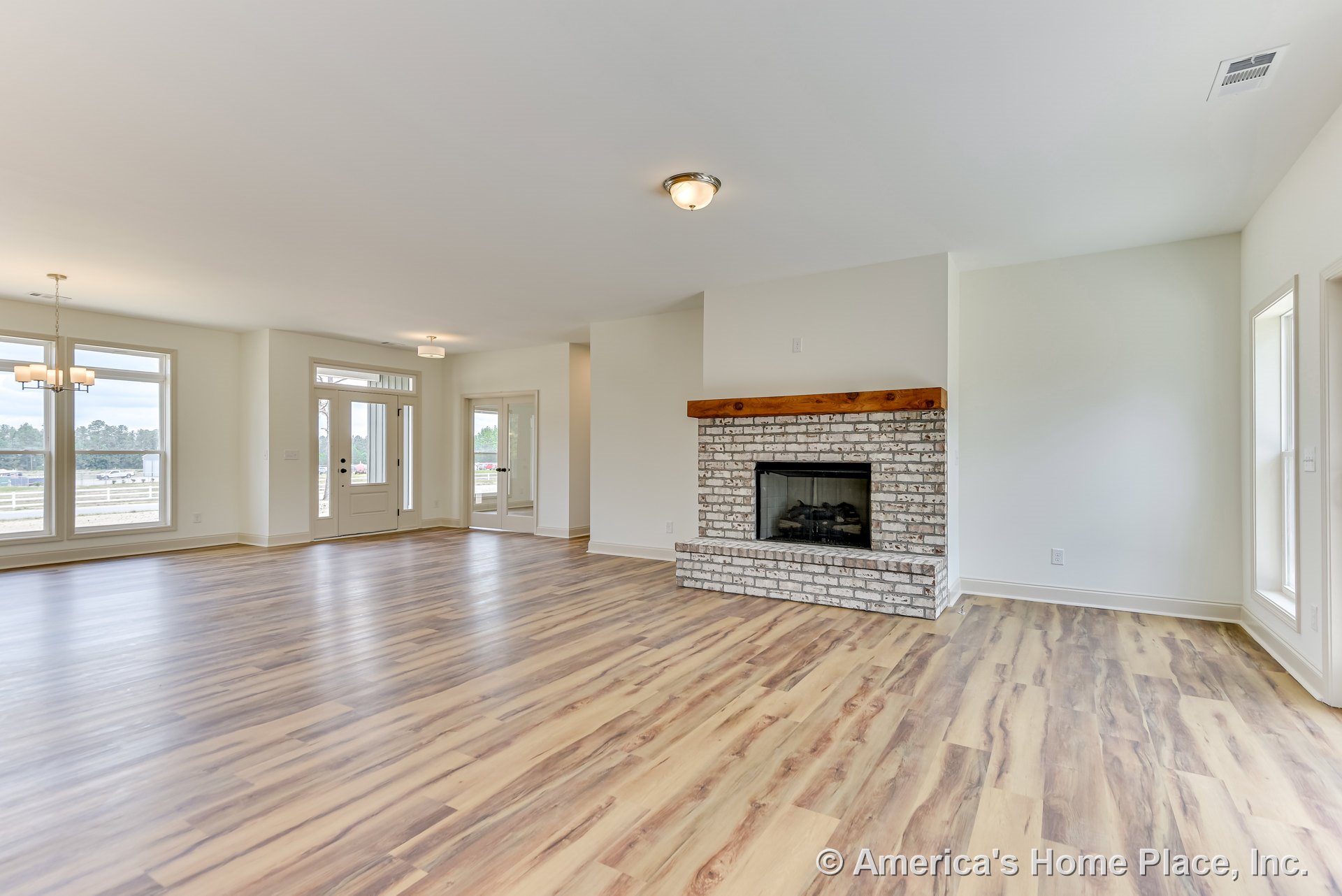 Open concept living room with whitewashed brick fireplace and wood mantel, wide plank wood-look flooring, large windows, recessed ceiling lighting, and adjacent dining area.