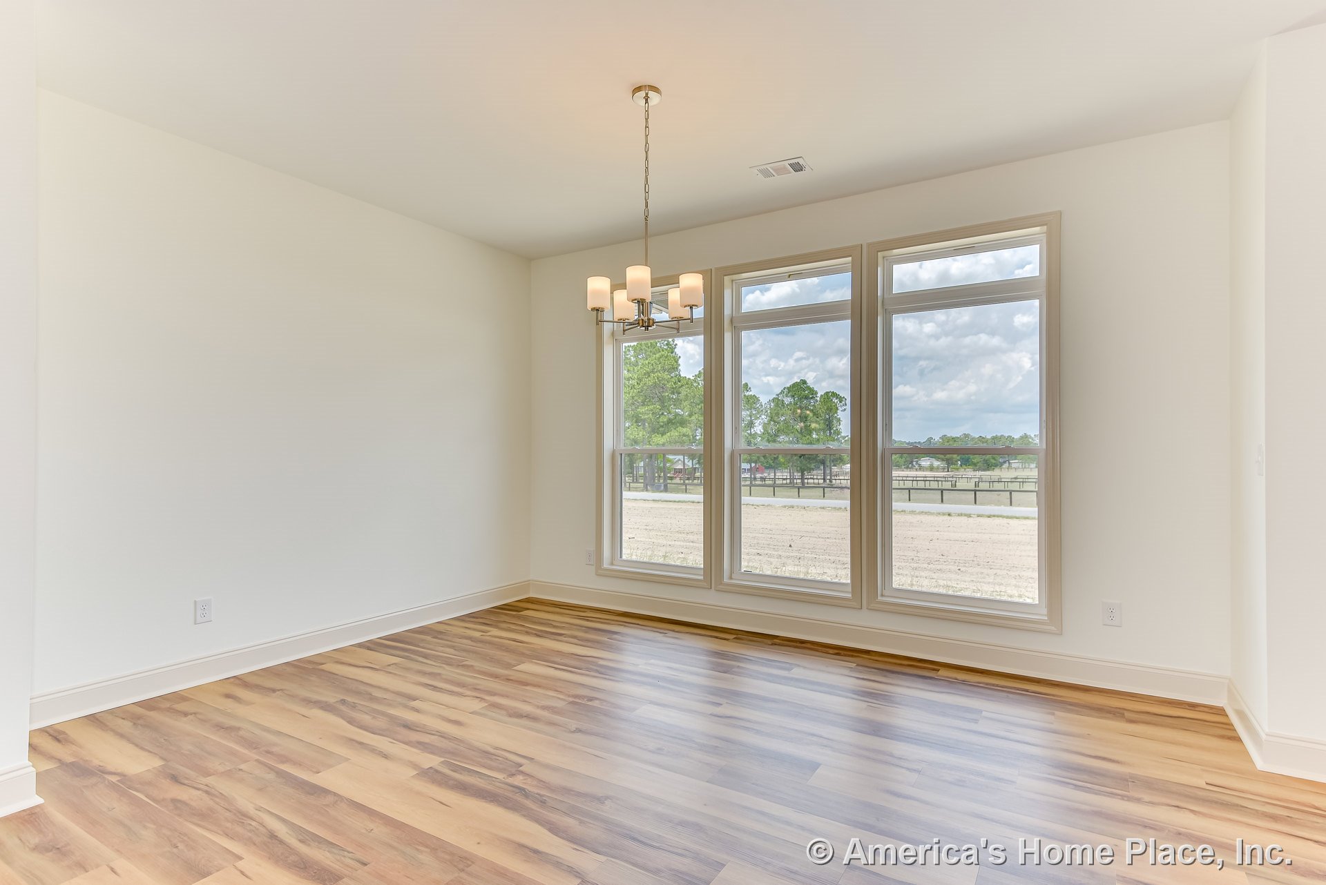 Dining room with triple picture windows, five-light modern chandelier, light wood laminate flooring, white walls and trim, rectangular layout, ceiling vent, and abundant natural