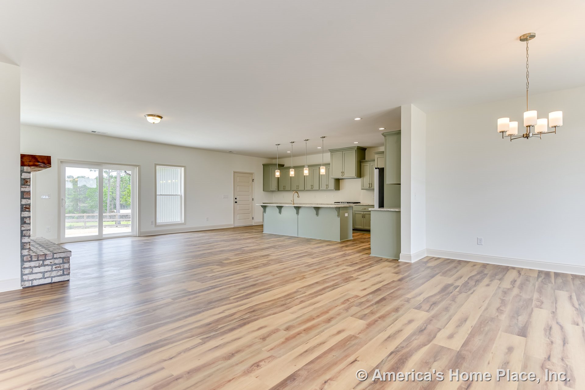 Open-concept living area with wood-look plank flooring, brick fireplace hearth, sage green kitchen cabinets, white quartz countertops, pendant lights above kitchen island