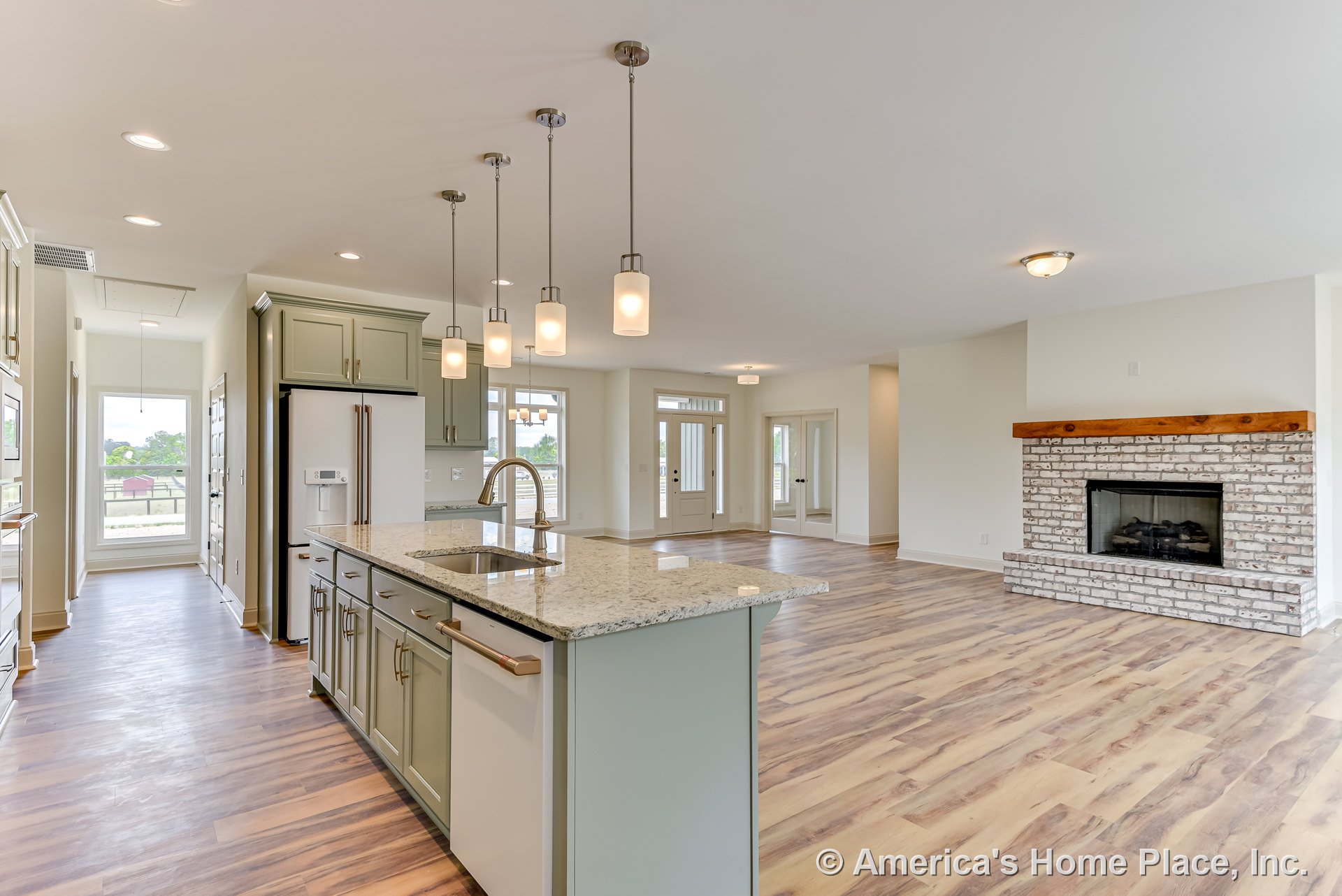 Granite kitchen island with pendant lighting, painted cabinetry, wide plank wood-look flooring, brick fireplace with wood mantel, large windows and glass doors in open floor plan.