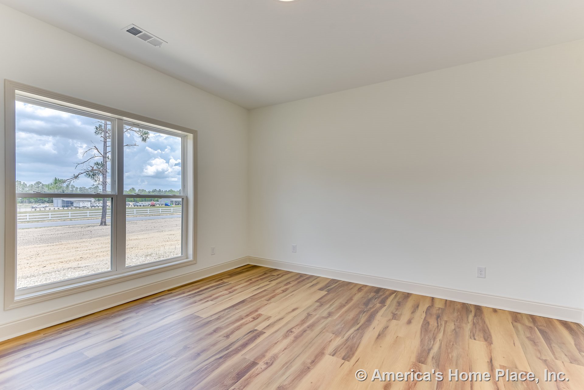 Bright bedroom with large double windows, wood-look laminate flooring, white walls, simple baseboard trim, ceiling vent, and recessed ceiling light.