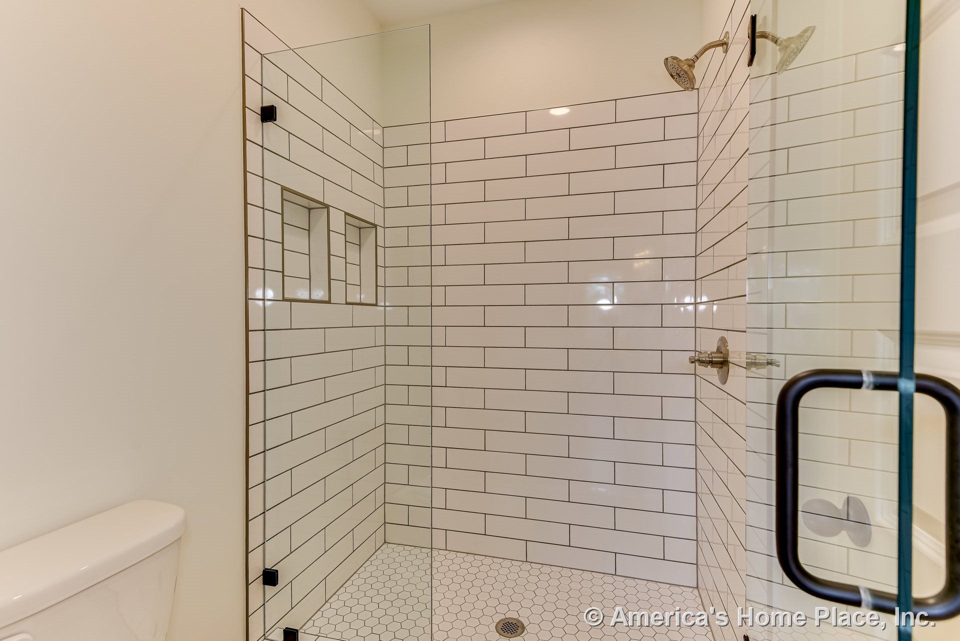 Walk-in shower with glass enclosure, dual metal shower heads, white subway tile walls, built-in niches, and hexagonal tile flooring