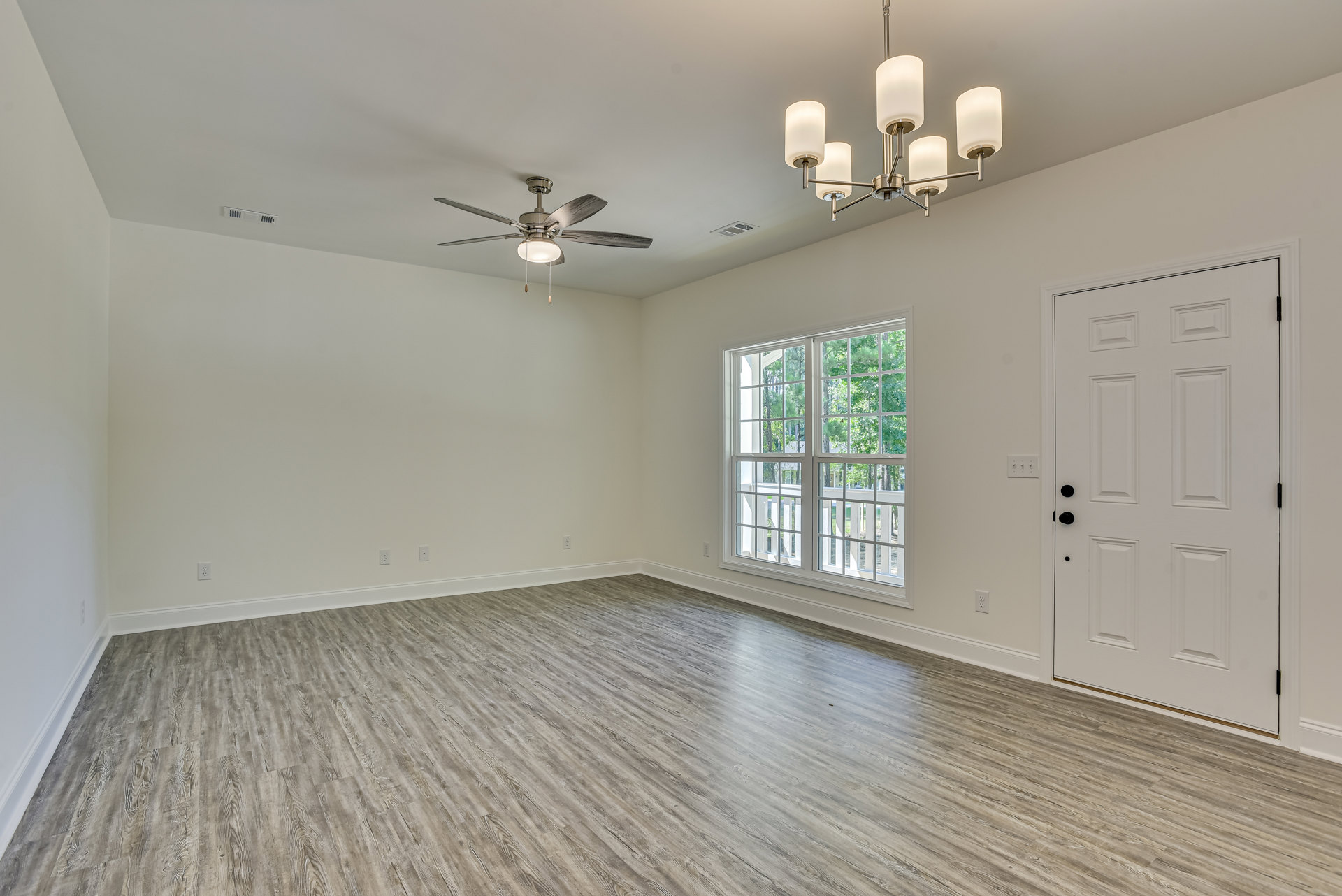 Wood flooring room with multi-pane window, white door featuring black hardware, ceiling fan with integrated light fixture, plaster walls and ceiling.
