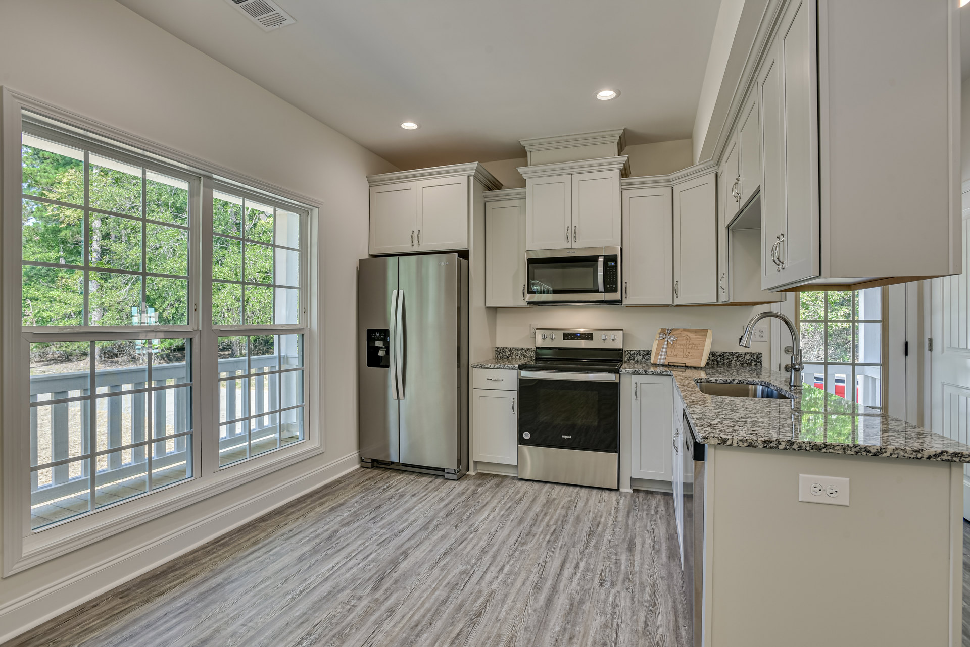 White kitchen cabinets and granite countertops, stainless steel refrigerator with water dispenser, black-top stove, white-door microwave, hardwood flooring, window overlooking deck