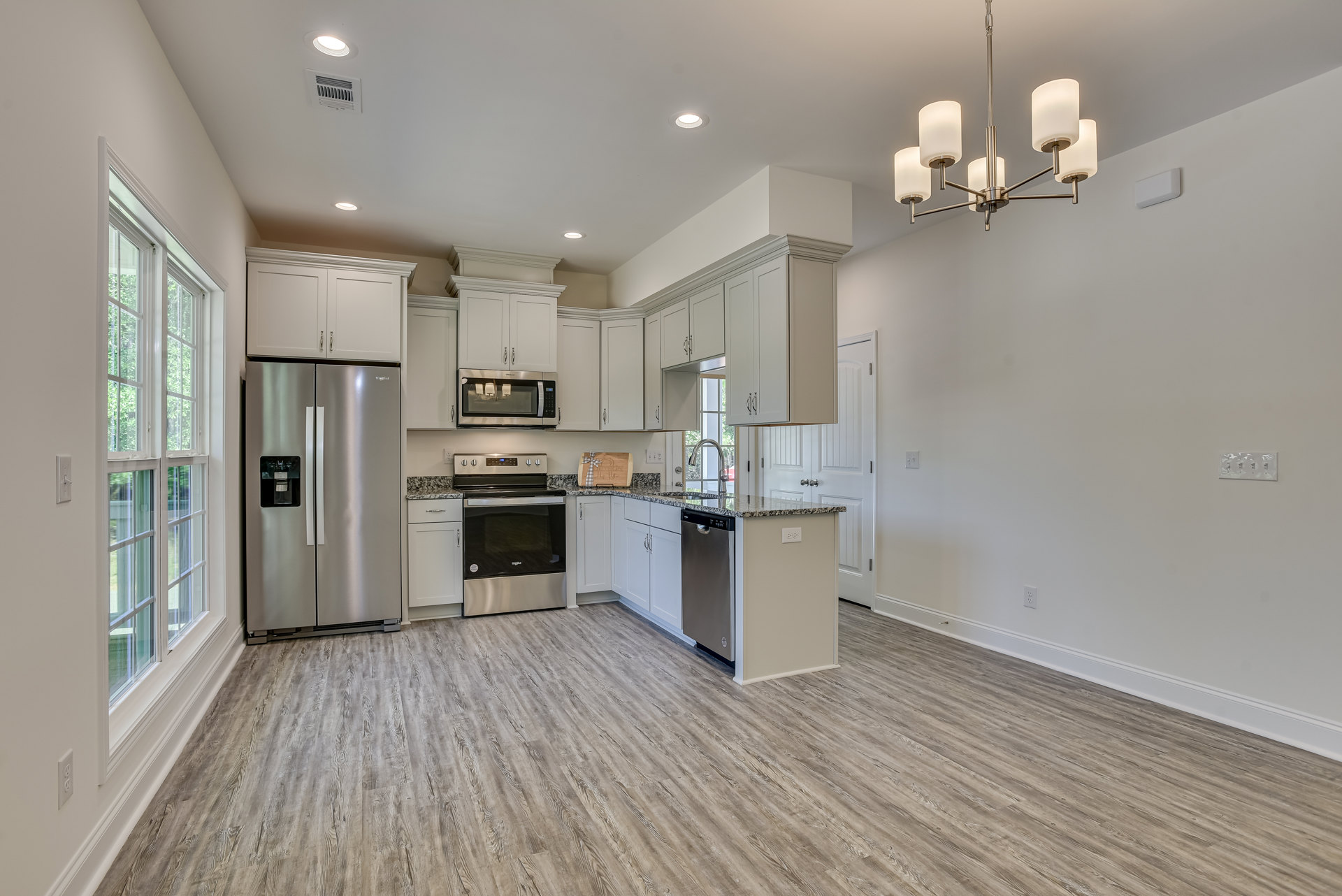 White kitchen cabinets, stainless steel appliances, wood flooring, stone countertops, and a wooden cutting board on the counter.