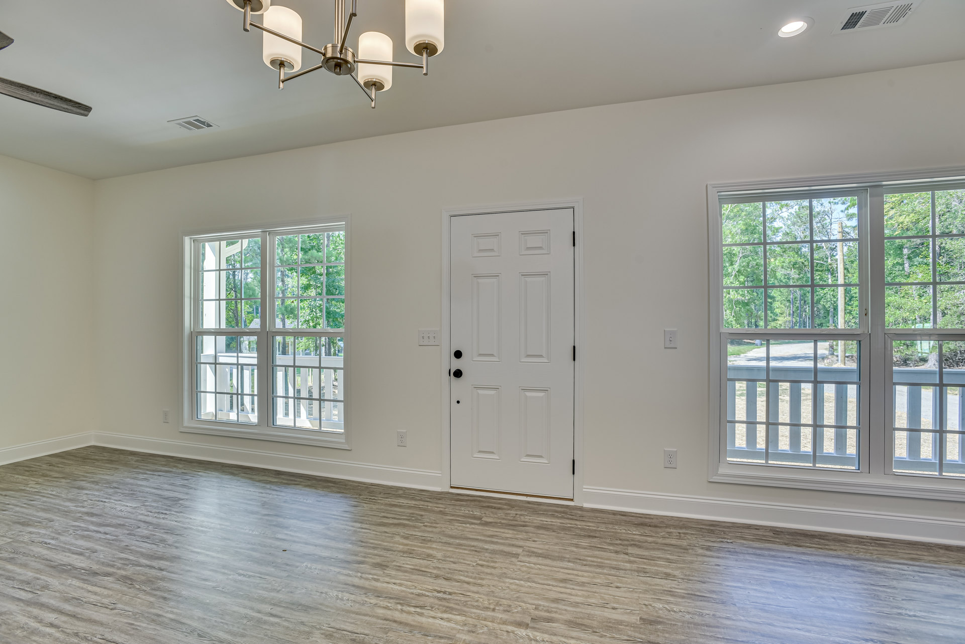 White paneled door with black hardware, wood flooring, ceiling light fixture, two windows showing trees and a garden path, white walls with crown molding