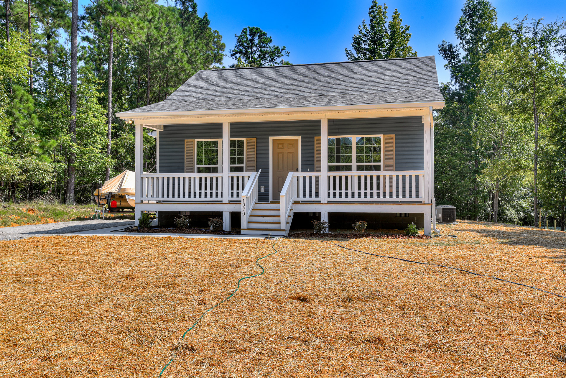 Two-story home with white siding, covered front porch, white railing, steps leading to entrance, green lawn, garden hose on ground, mature trees in yard, large windows, blue sky