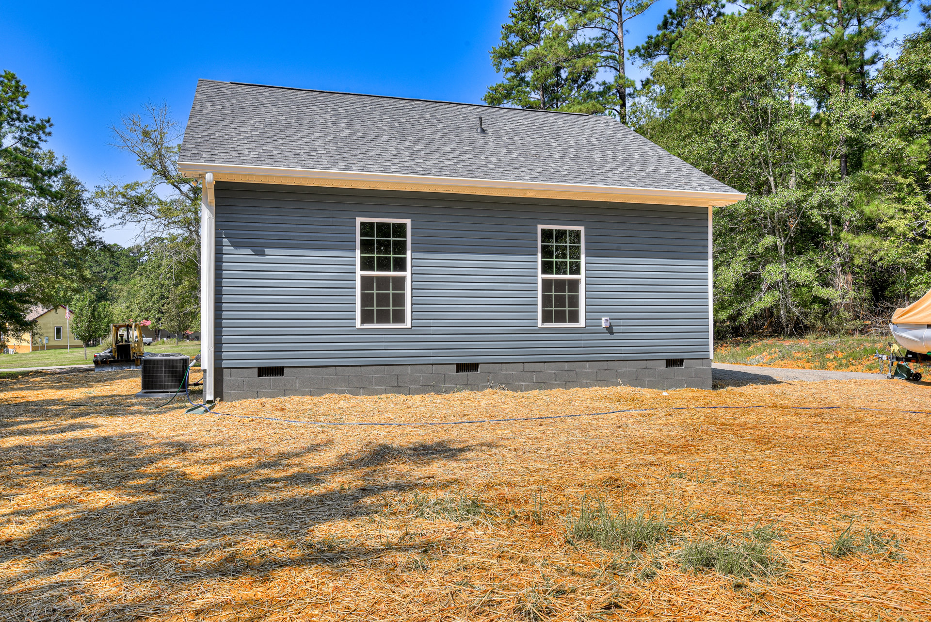 Blue-roofed house with white and green framed windows, surrounded by tall trees; black metal box with hose and yellow tarp covering a boat in the yard.