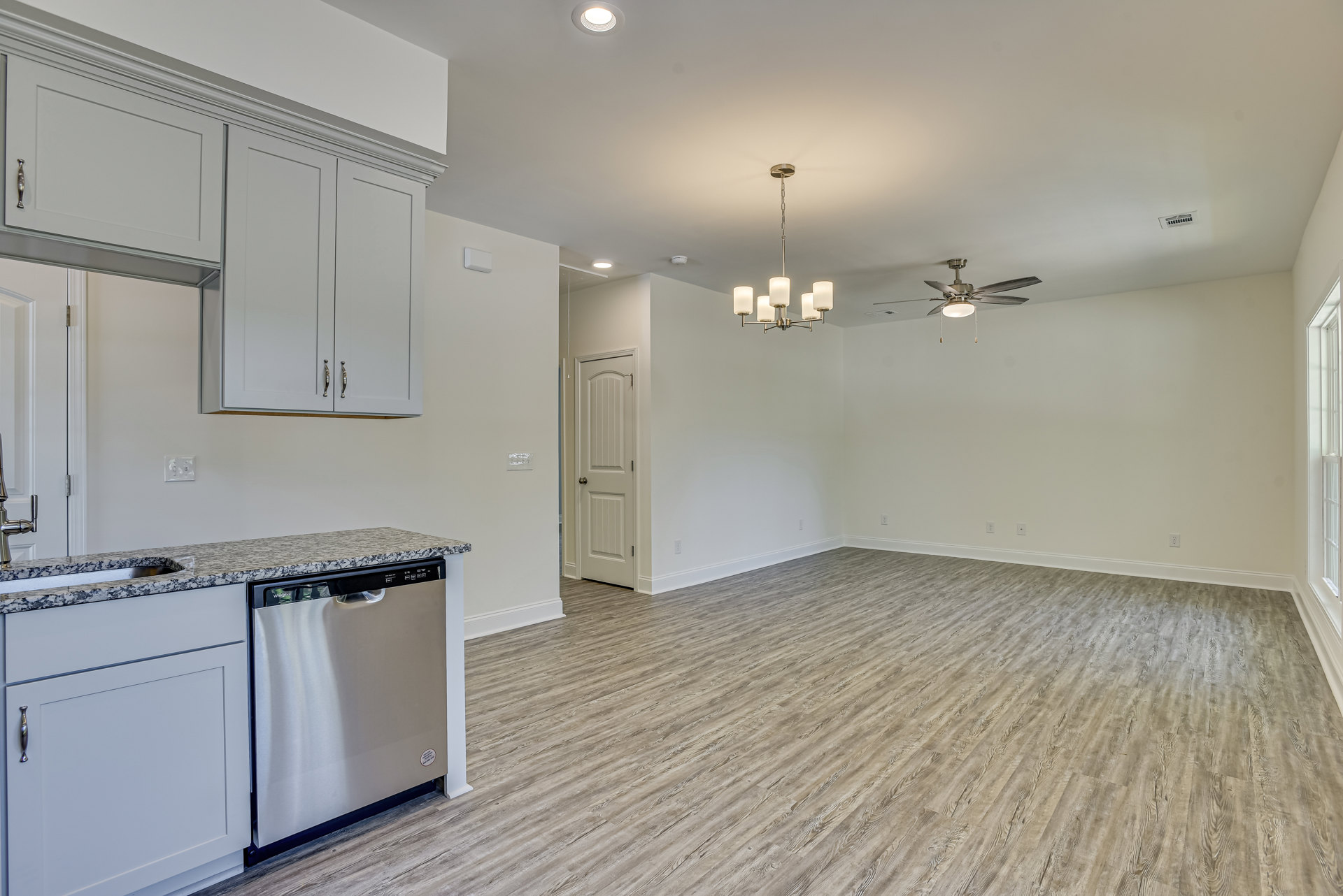 Stainless steel dishwasher with black handle beside white cabinet topped with marble, wood flooring, and silver doorknob on adjacent white door