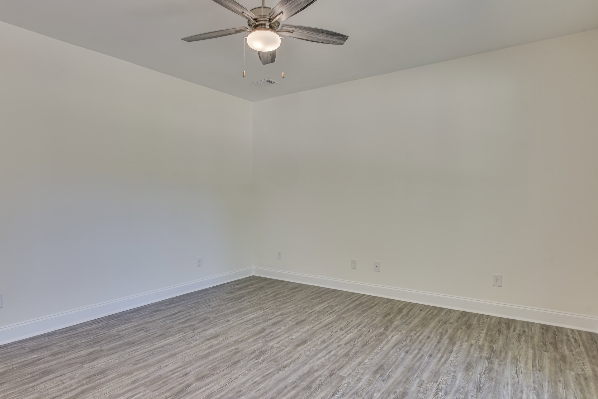 Ceiling fan with integrated light fixture mounted on white plaster ceiling above wood flooring and white walls in residential interior.