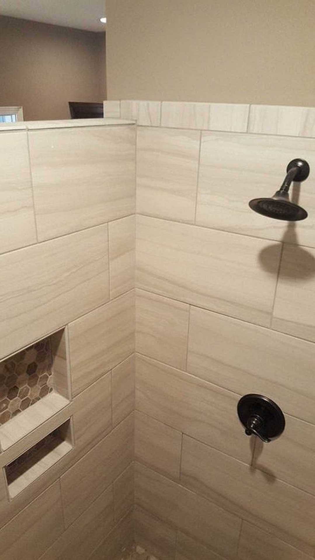 Walk-in shower featuring a tiled wall with a built-in niche holding soap, round shower head, and partial view of toilet and floor tiles