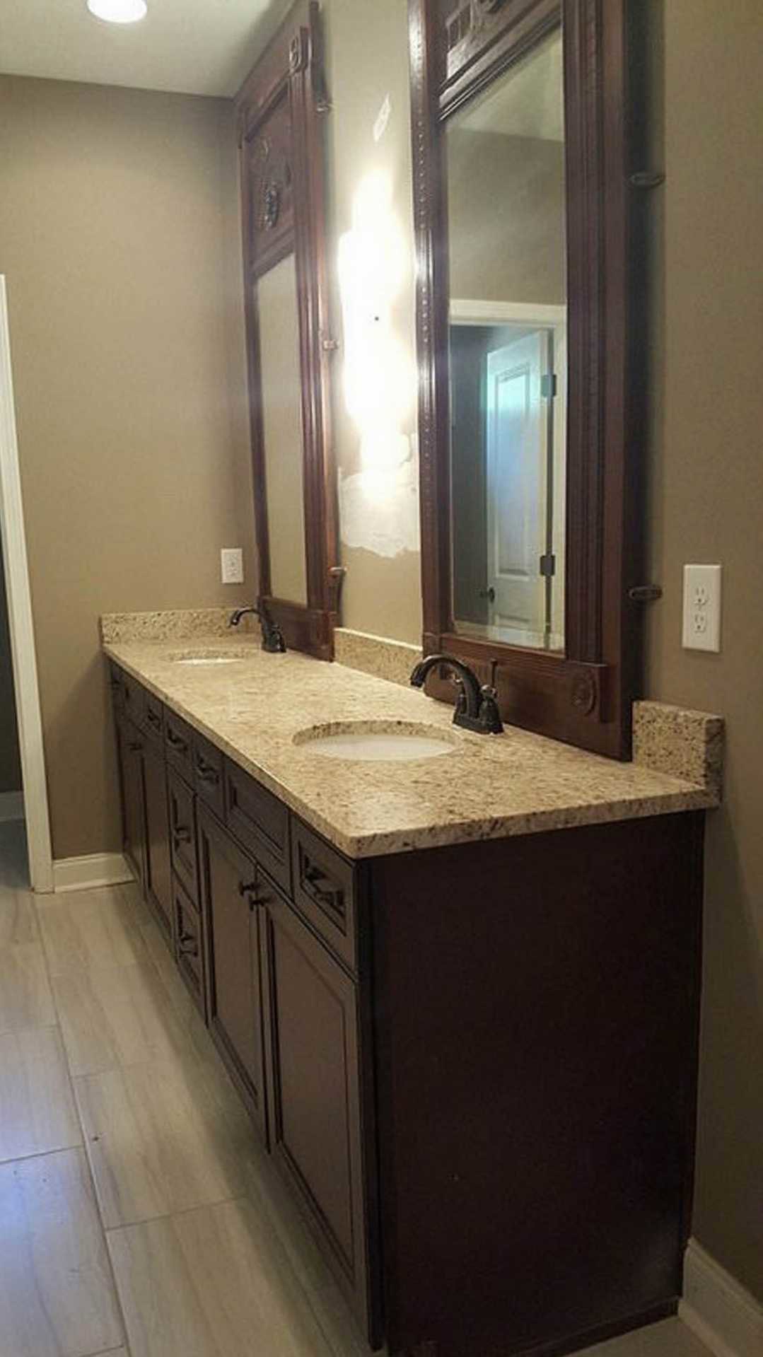 Bathroom with two rectangular mirrors above double sinks, stone tile wall, white countertops, chrome faucets, dark wood cabinetry, and visible electrical outlet.