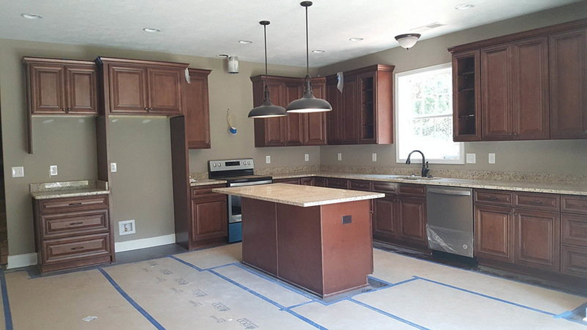 Marble kitchen island with built-in sink, white cabinetry, stainless steel appliances, gold-framed wall art, pendant lighting, and sunlight streaming through window
