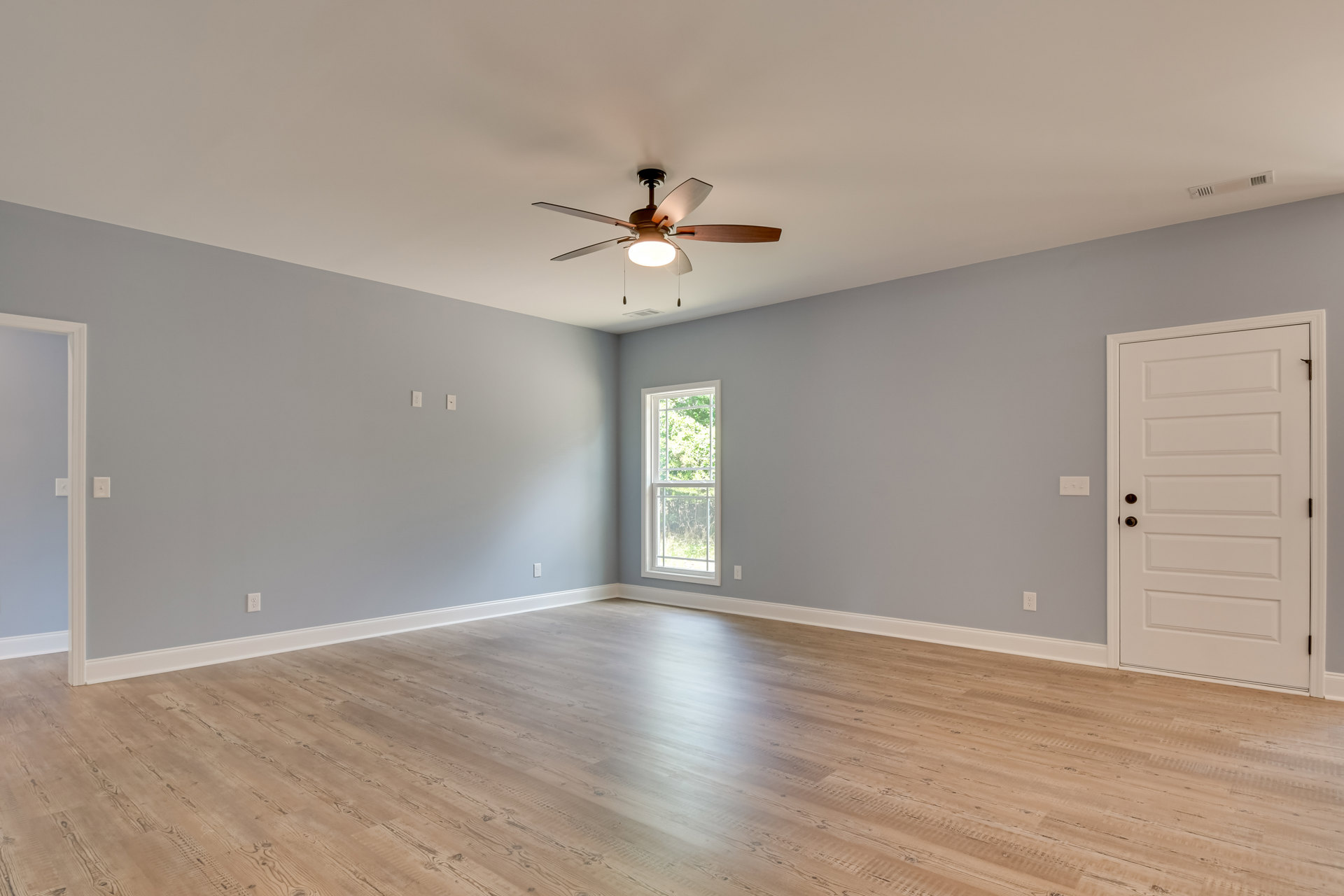 Hardwood flooring, white walls, ceiling fan with light fixture, white-framed window, white door with silver doorknob