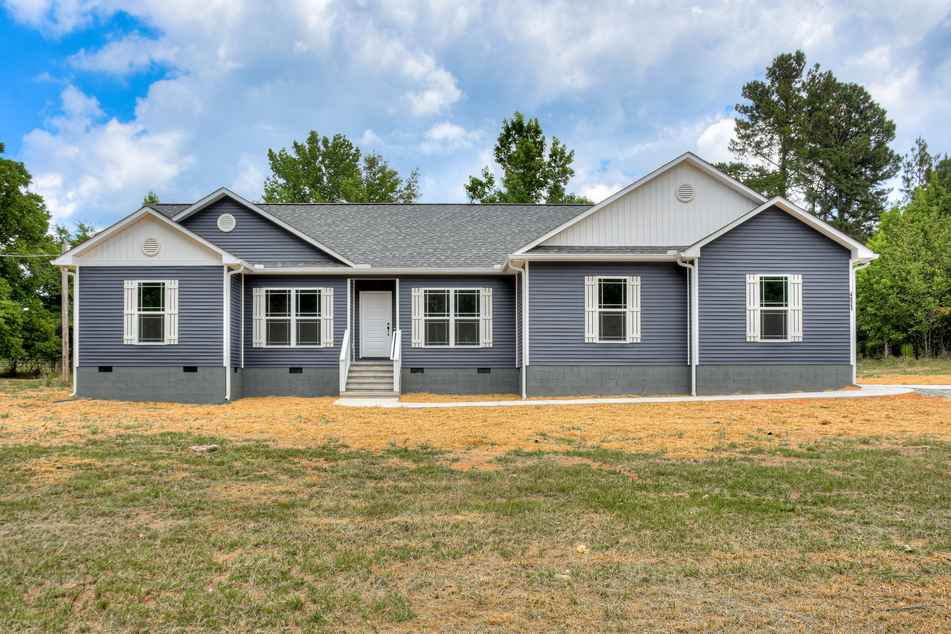 Two-story house with white trim windows, white shutters, white front door, covered porch, green lawn, and mature trees in the background