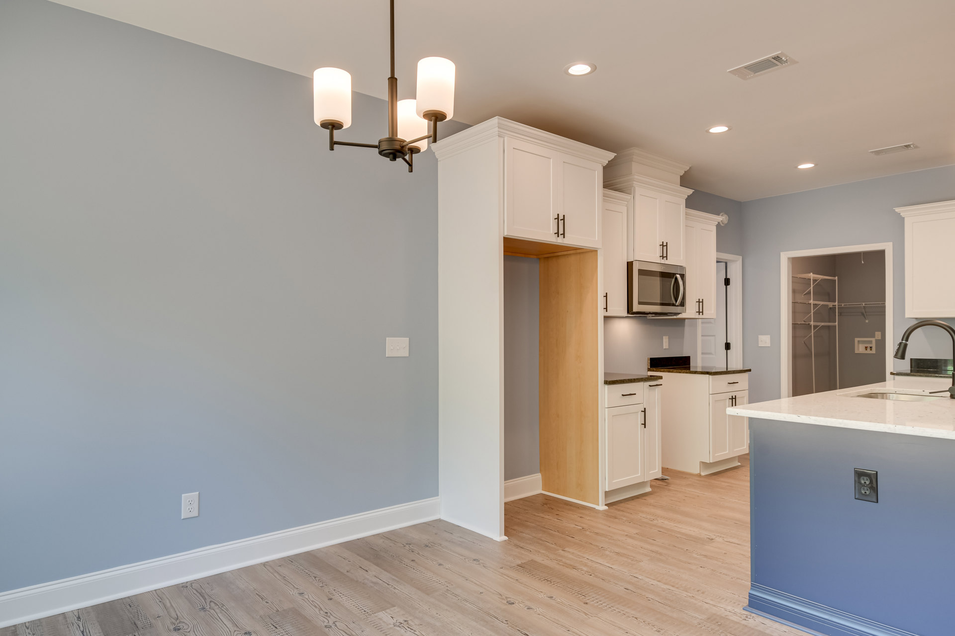 Kitchen with wood flooring, central island featuring a sink and electrical outlet, white cabinetry with black handles, built-in microwave oven, white round light fixture, and white