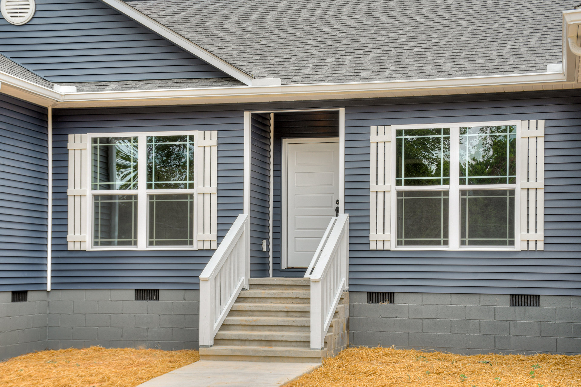 White front door and stairs leading to entry porch, white-framed sash windows, gray shingle roof, screened side window, exterior vent, light-colored siding
