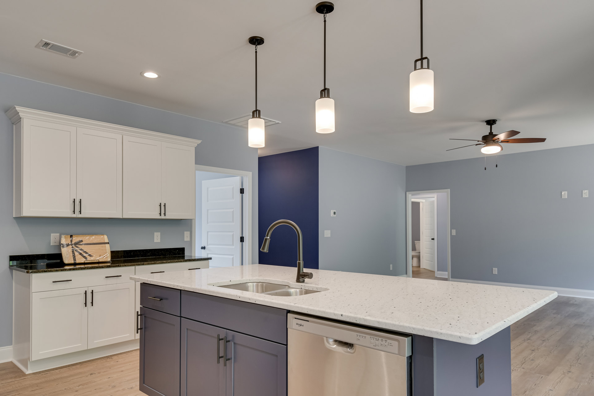 Modern kitchen featuring white cabinetry, stainless steel sink with chrome faucet, built-in dishwasher, stone countertop, and recessed lighting.