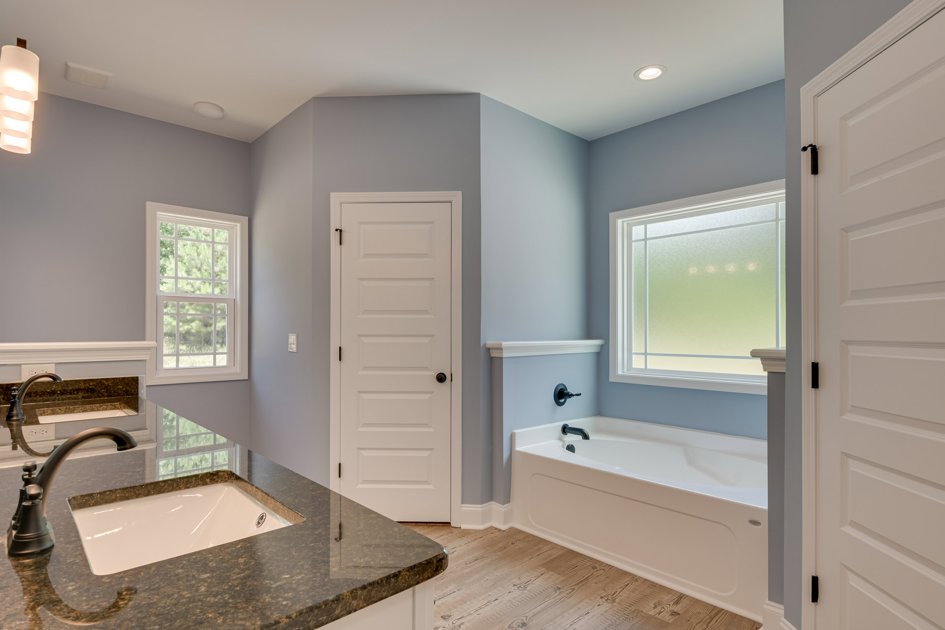 Bathroom with white freestanding bathtub and black faucet, marble countertop sink, frosted glass window, white door with black handle, and close-up of modern light fixture