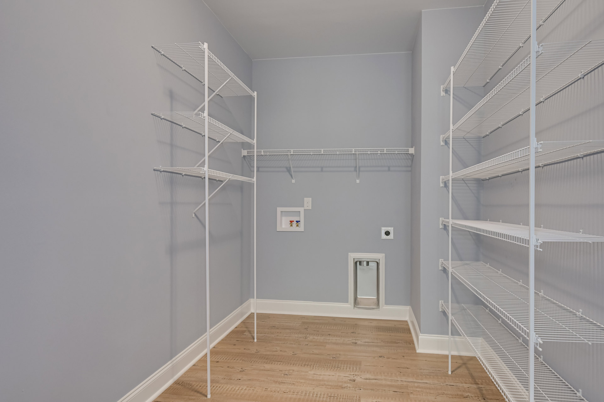 Empty closet with white shelves, wood floor, and built-in dog door on one wall